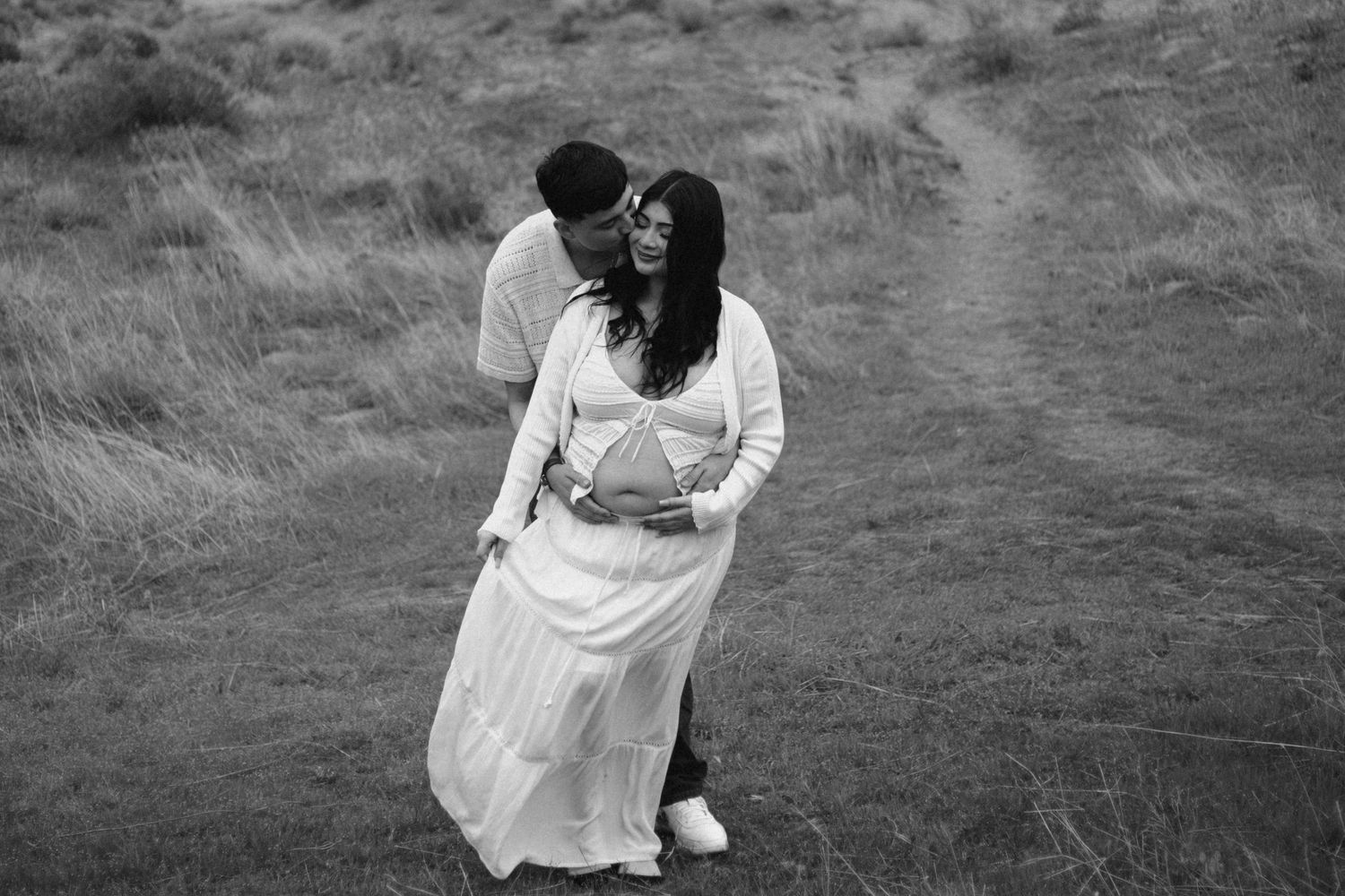A romantic black and white photograph showing an intimate moment between a couple in a grassy field.