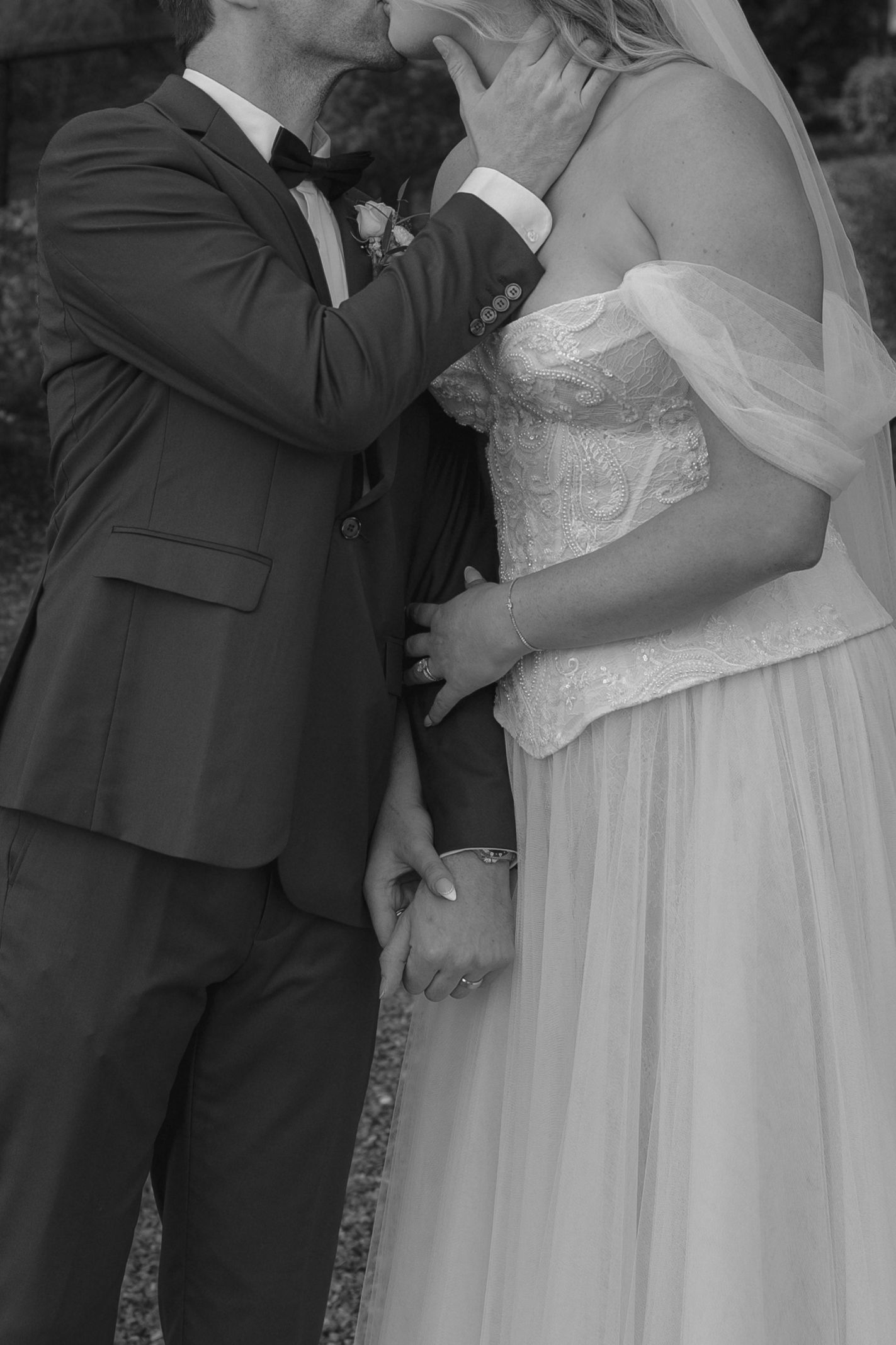 Black and white photo of a bride and groom holding hands and sharing a tender moment on their wedding day.
