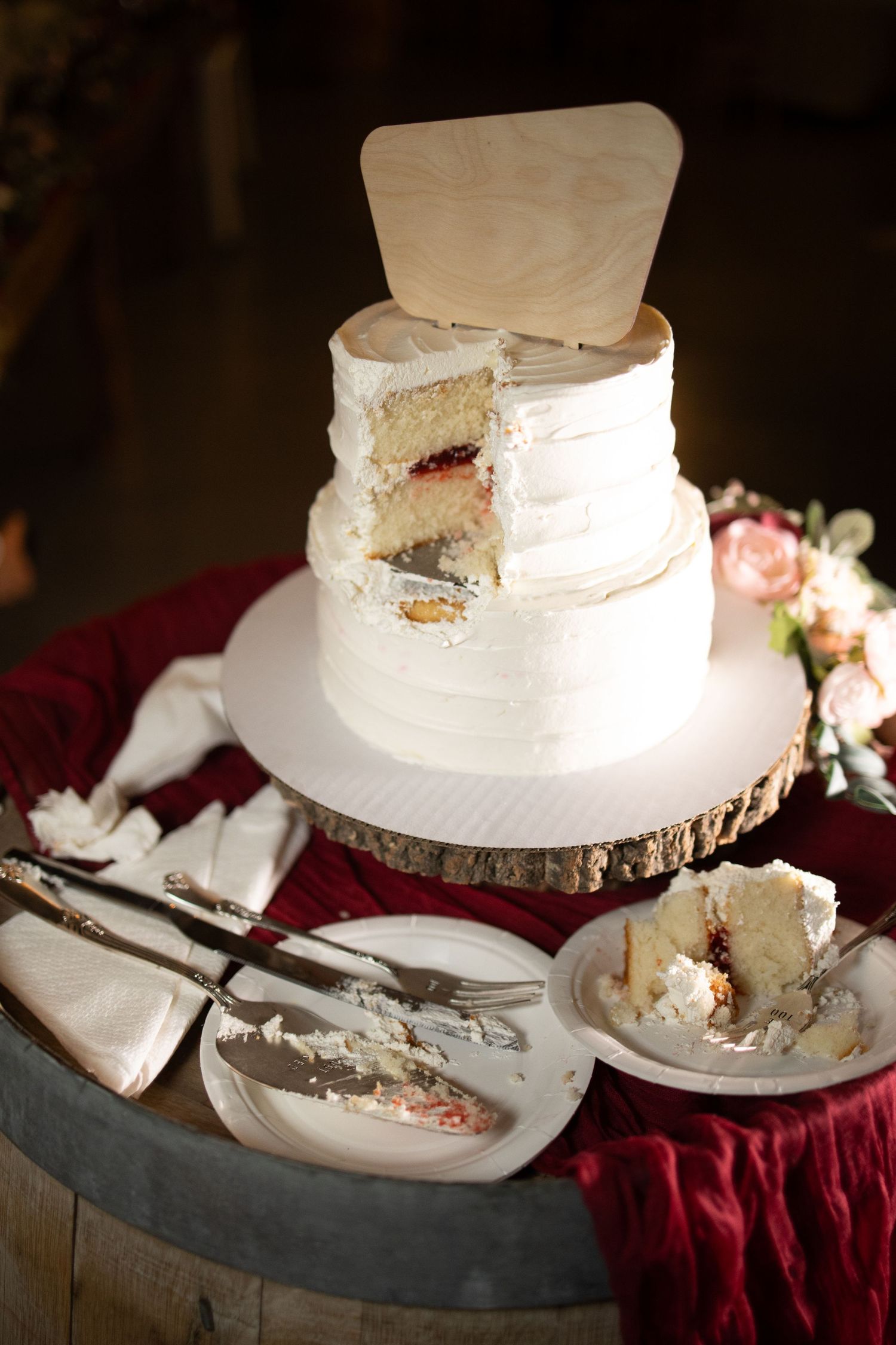 White wedding cake slices on plates displayed on a burgundy tablecloth with rustic wooden accents.