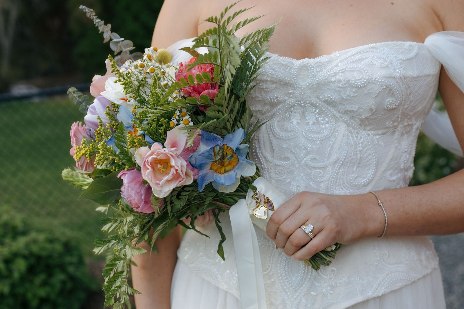Bride in white strapless lace gown holding colorful wedding bouquet with pink, blue flowers and ferns.