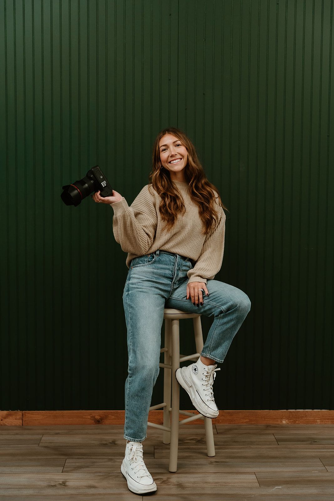 Casual lifestyle portrait series showing someone in blue jeans and white sneakers seated against a dark green wall.