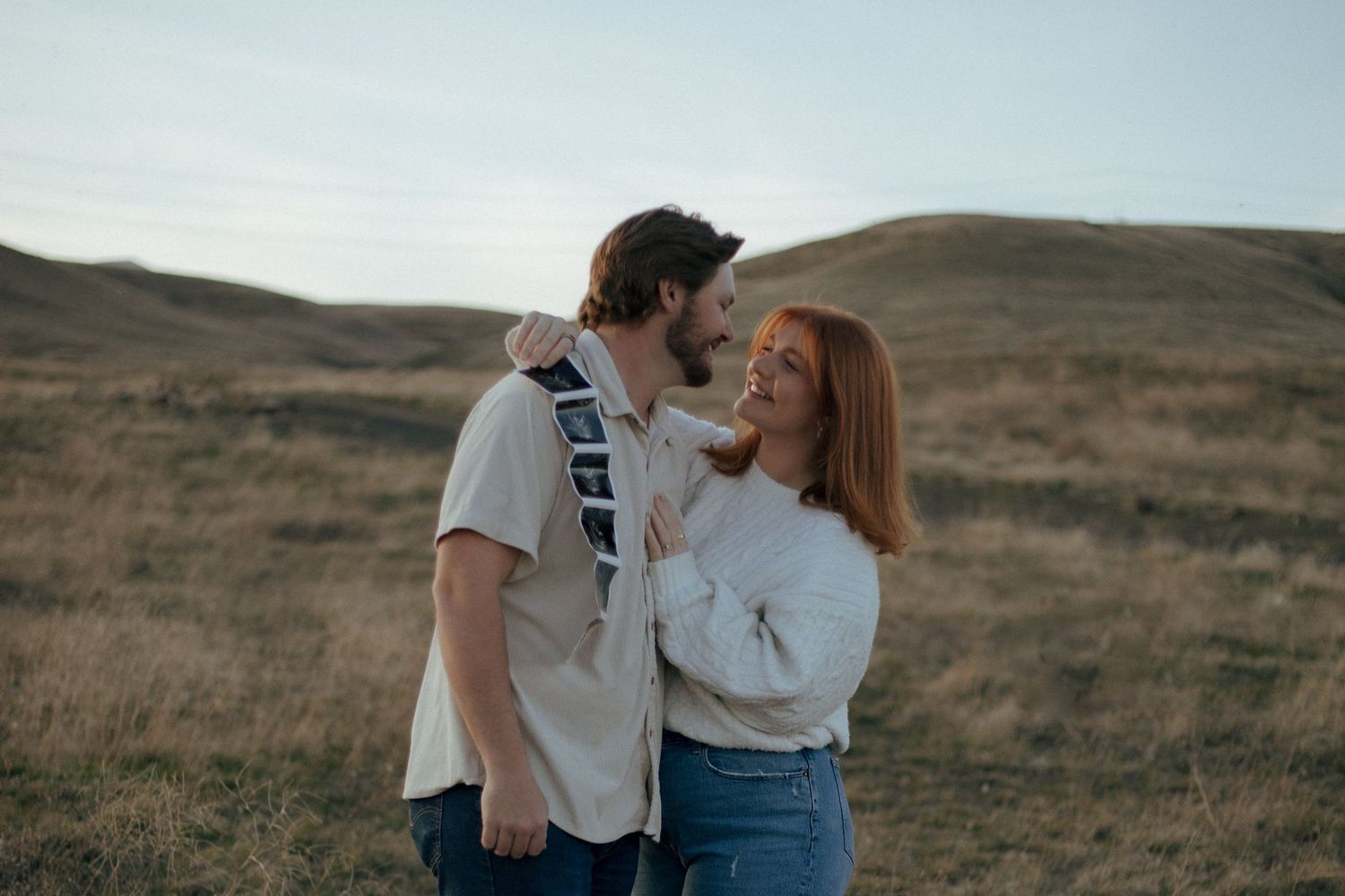 A loving couple shares an intimate moment together in a serene mountainous landscape at dusk.