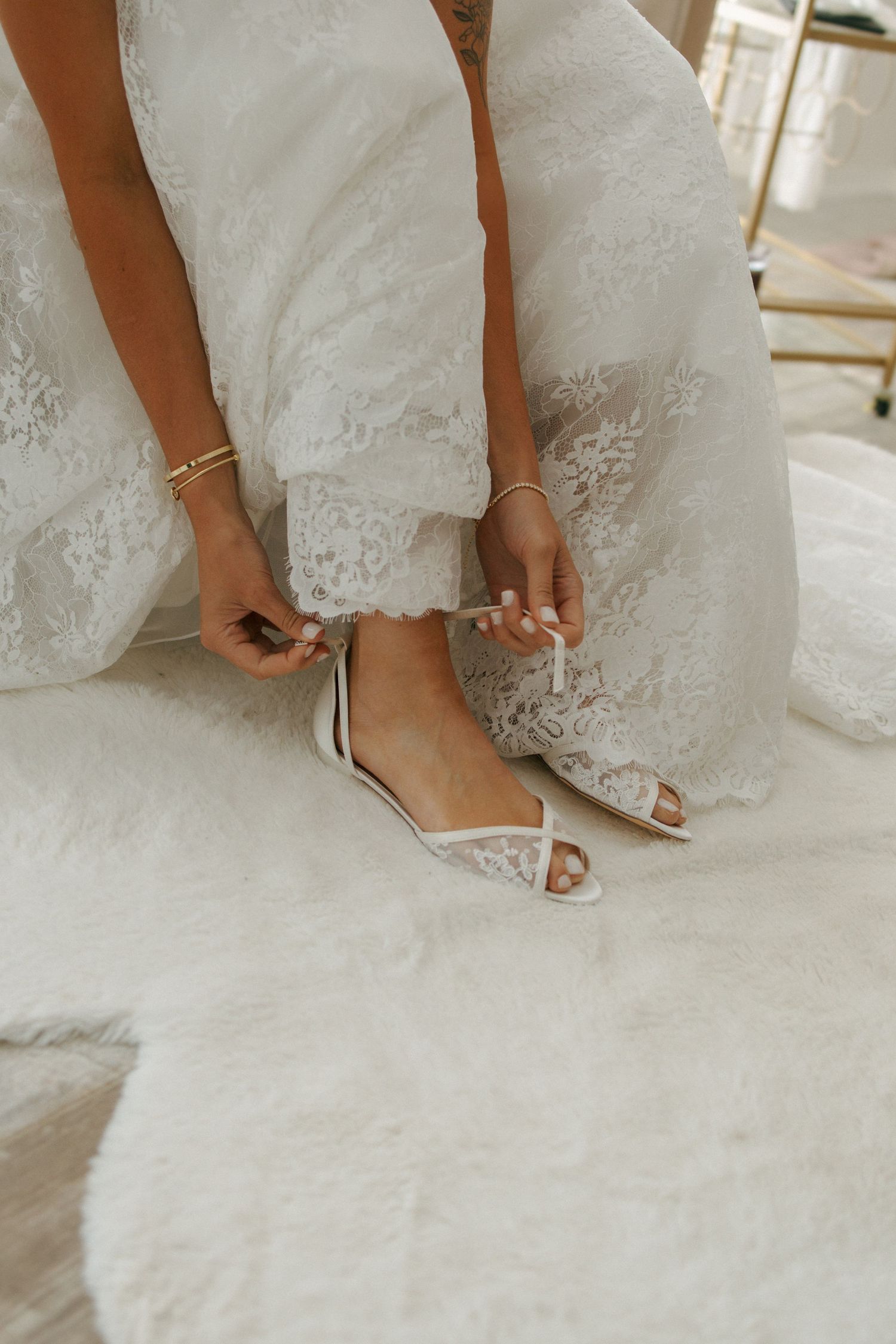 Close-up of bride wearing delicate white lace wedding dress and elegant peep-toe flat sandals.
