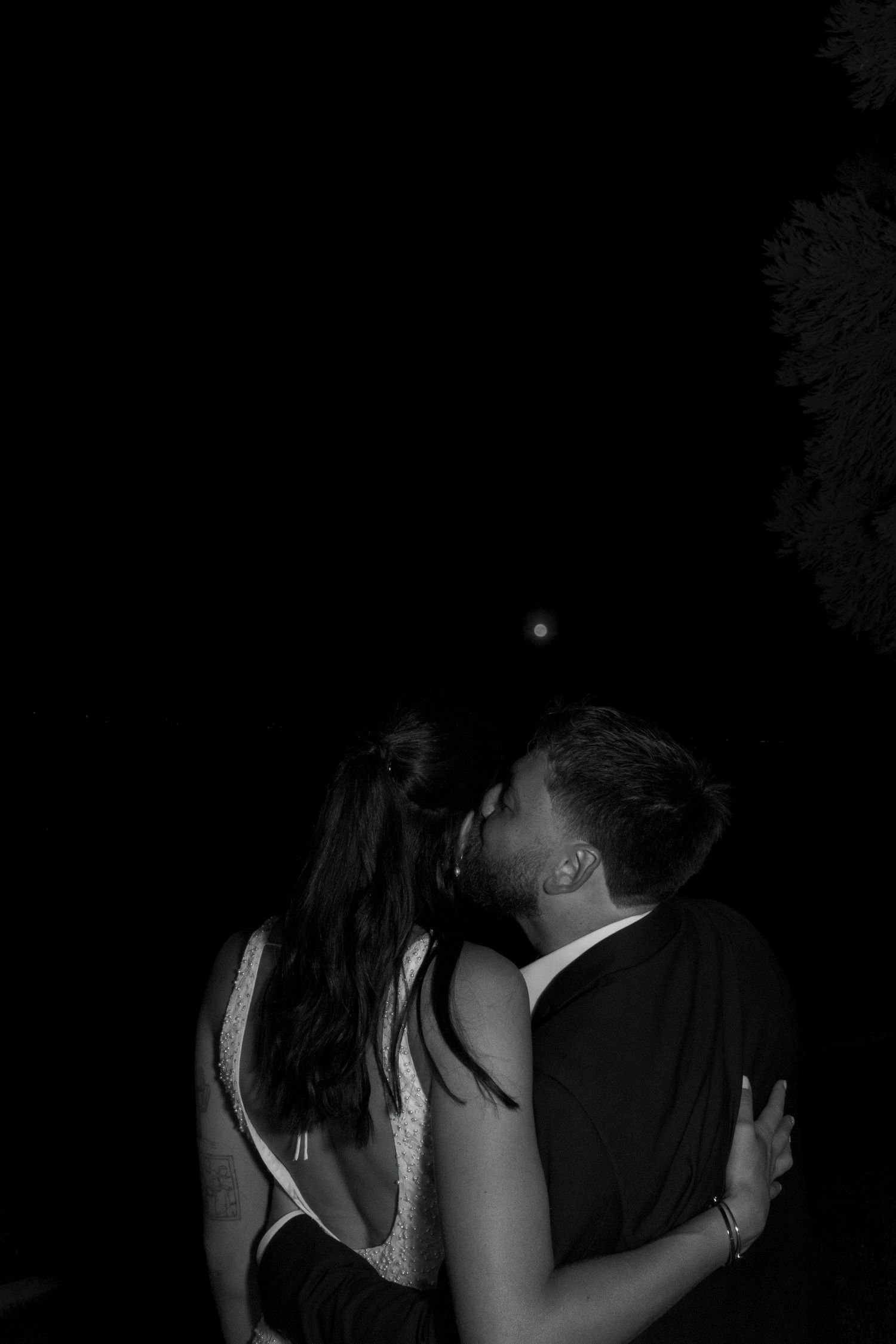Black and white nighttime photo of a couple sharing an intimate kiss during their wedding reception.