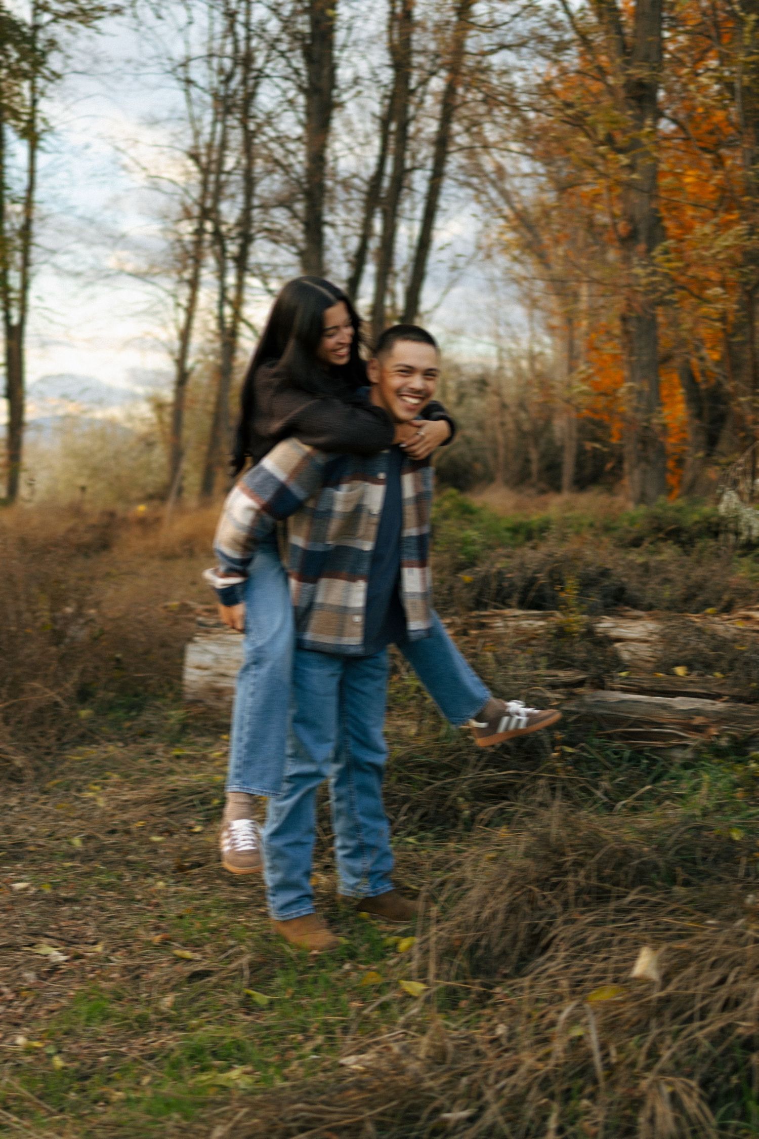Person in jeans and blue jacket bends down to collect sticks and branches in autumn forest setting.