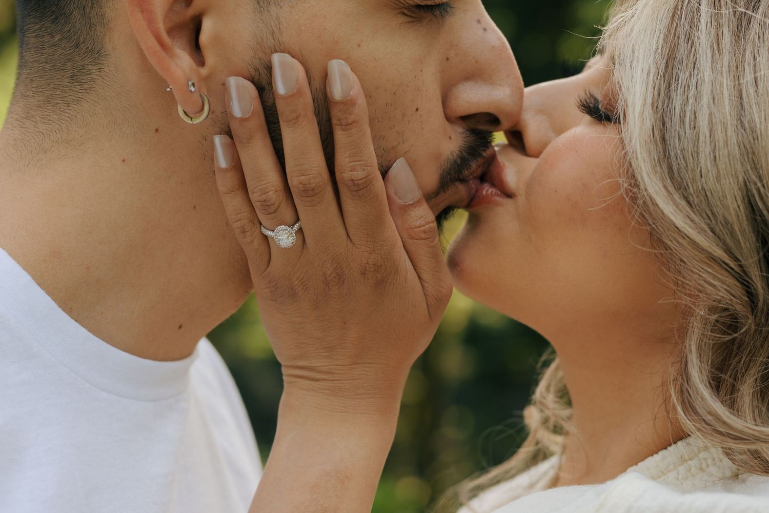 Close-up of a couple sharing a romantic kiss, woman wearing a diamond engagement ring touching man's face.