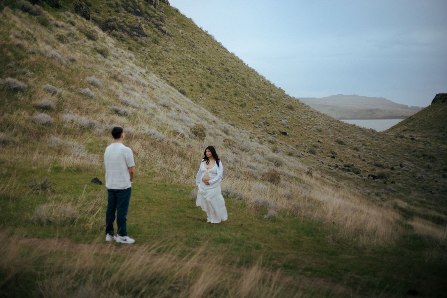 Two people standing on a grassy hillside overlooking misty mountains in a moody landscape.