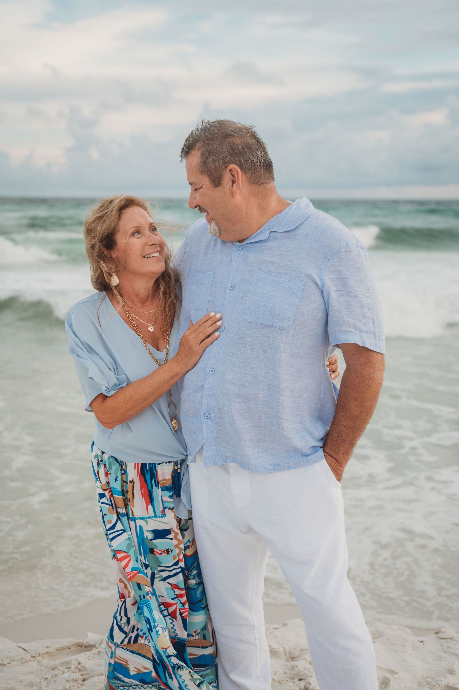 A happy couple shares a joyful moment together while standing on a beach with ocean waves in the background in Panama City Beach.