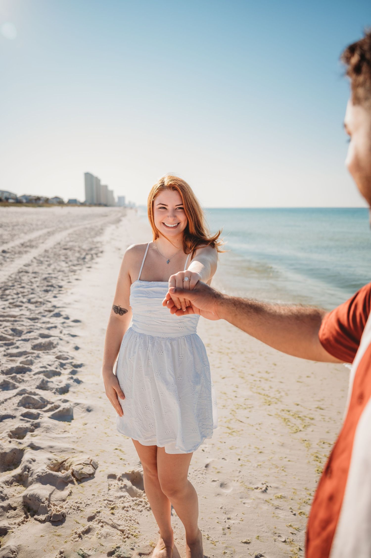 Woman in white summer dress shows off her new engagement ring after a surprise proposal in Panama City Beach.