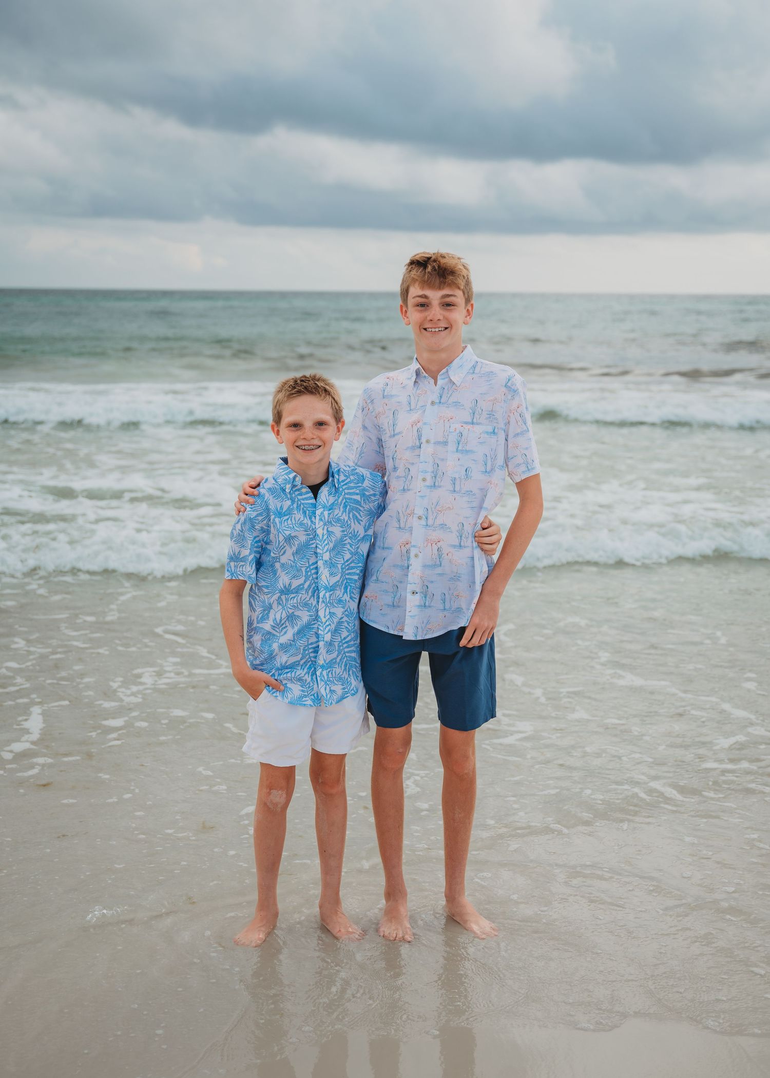 Children stand together at the beach's edge with waves and cloudy skies in the background in Panama City Beach.