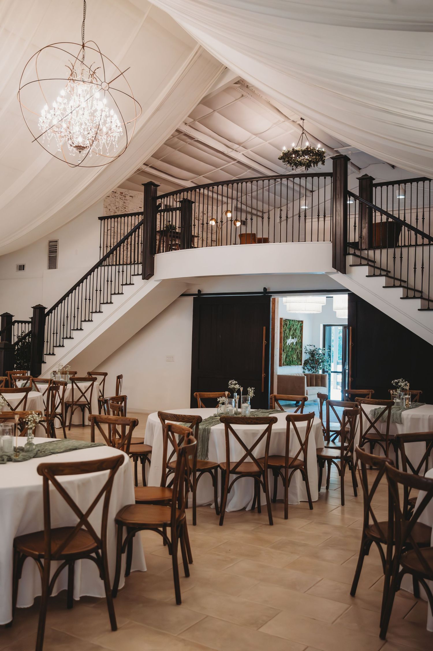 Elegant wedding venue interior with draped ceiling, crystal chandelier, crossback chairs and split-level dining space at a 30A wedding.