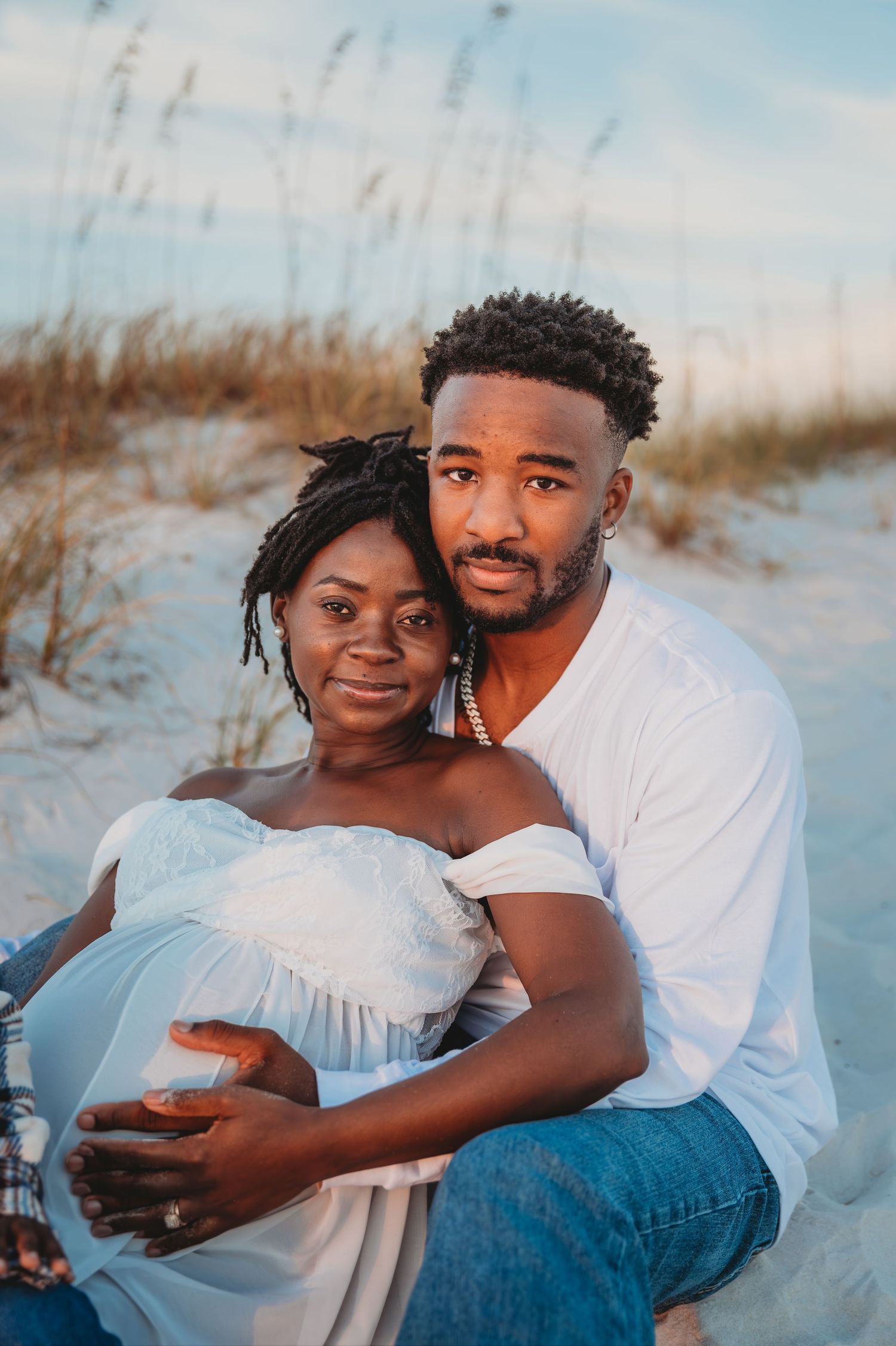 A couple shares tender moments together while sitting on a sandy 30A beach at sunset.