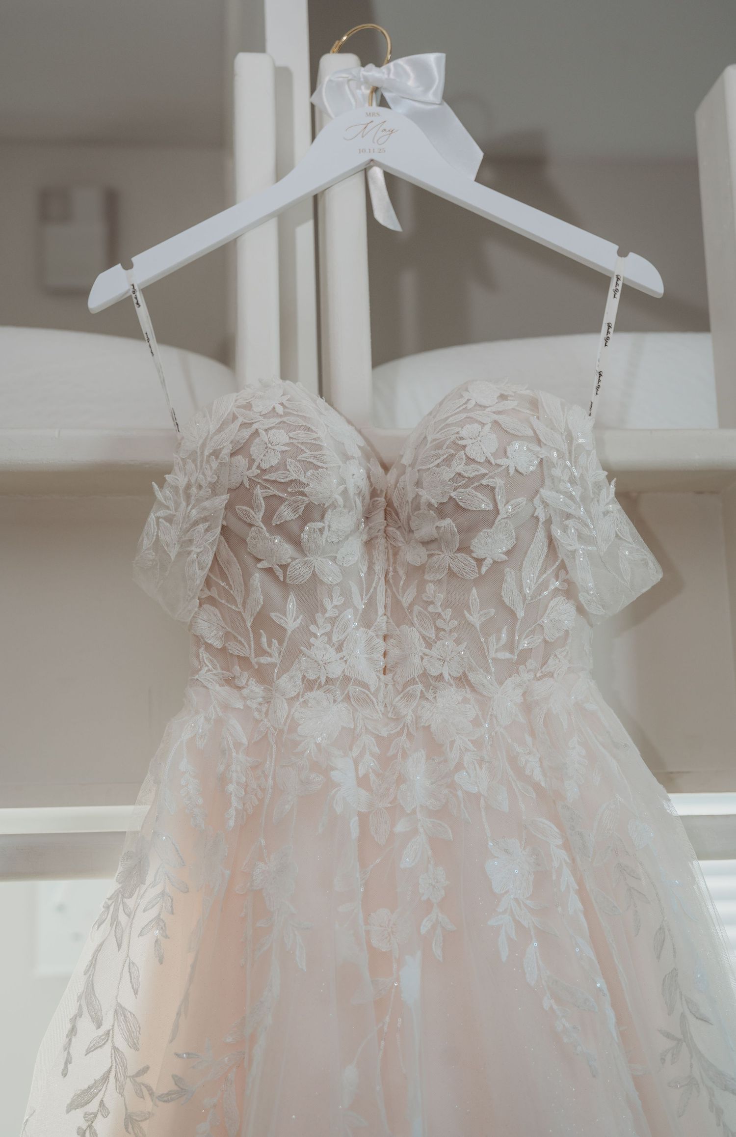 A delicate blush wedding dress with intricate lace details and sweetheart neckline hangs on a white hanger during a 30A wedding.