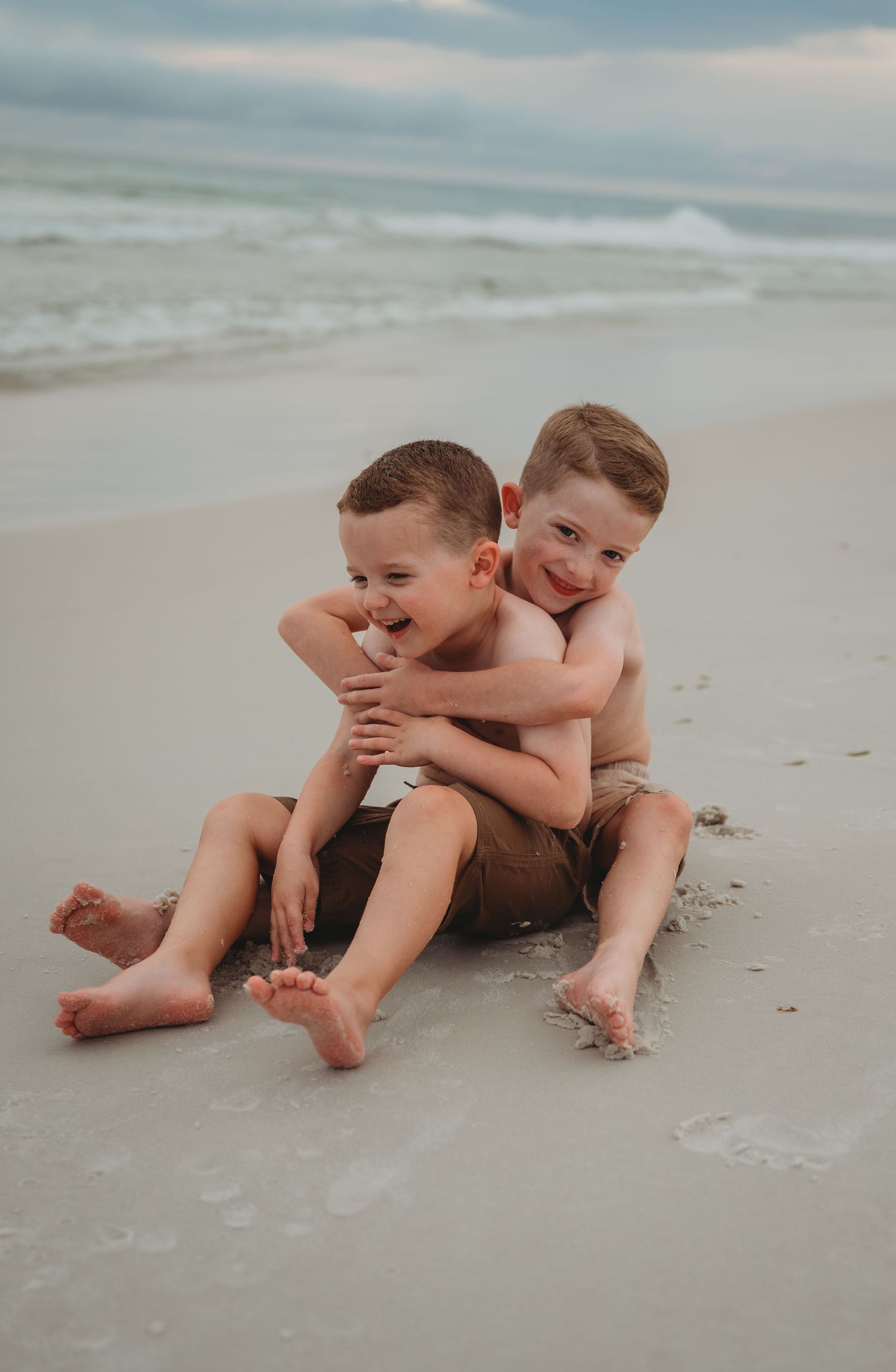Playful moments captured of two young siblings laughing and rolling in the white sand at the beach in Panama City Beach.