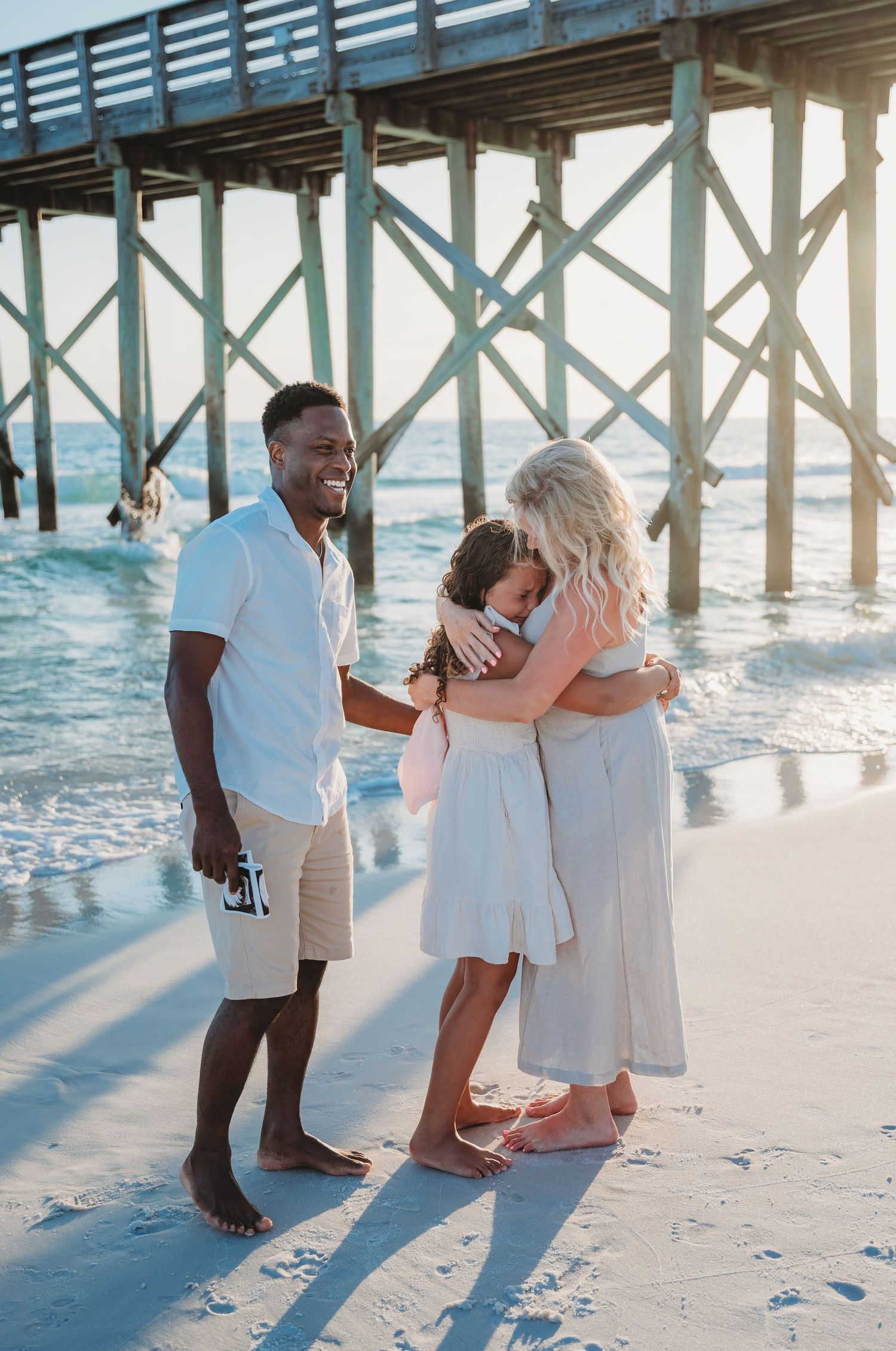 Happy people dressed in white hugging under a wooden pier in Panama City Beach.