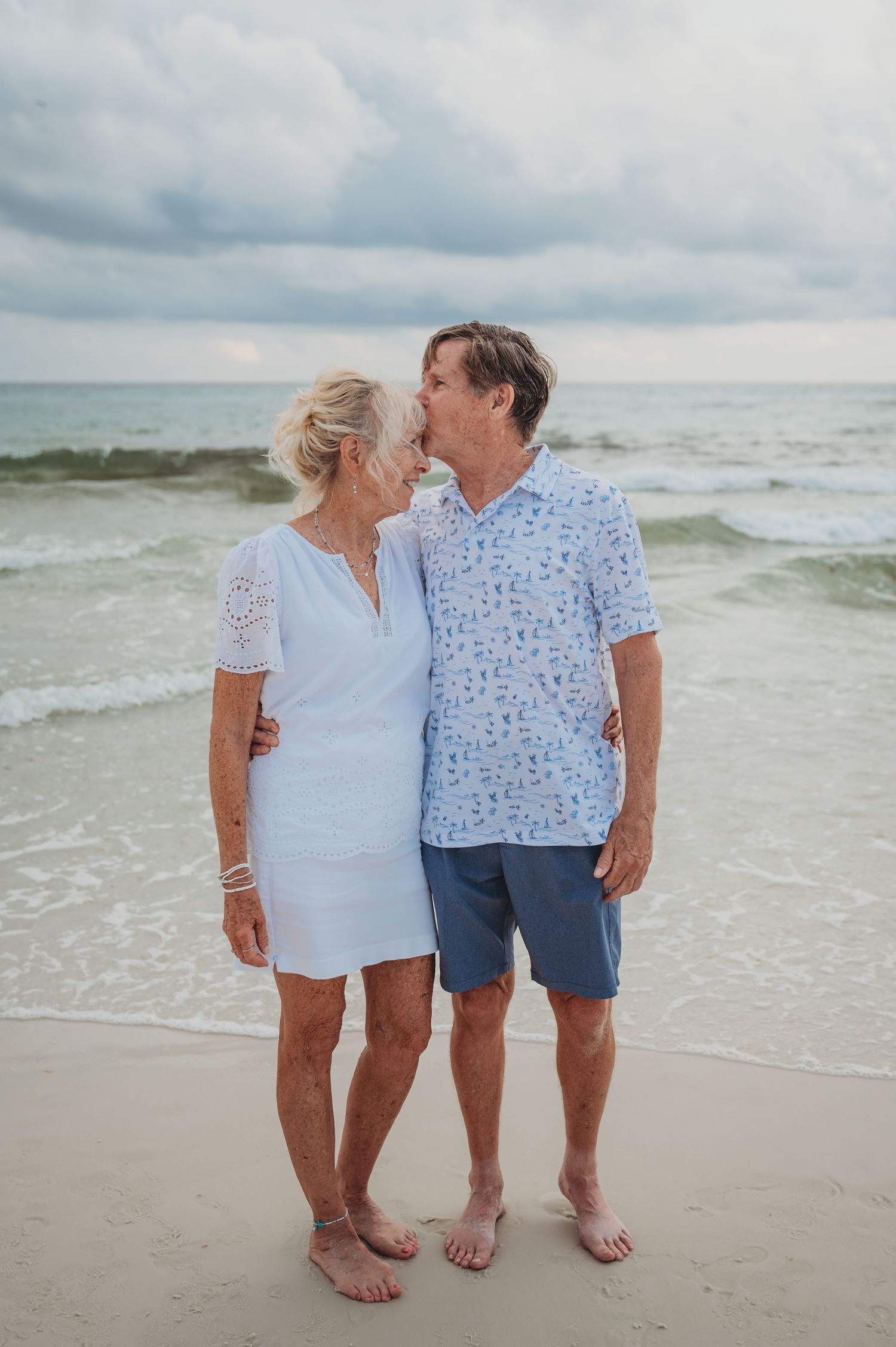 Couple in matching blue and white outfits walking along serene beach shore during cloudy day in Panama City Beach.