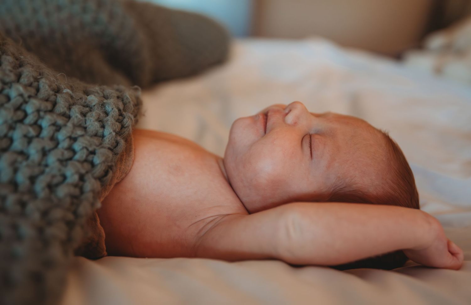 A sleeping baby wrapped in a cozy gray knitted blanket rests peacefully on soft bedding during a newborn session in Panama City.