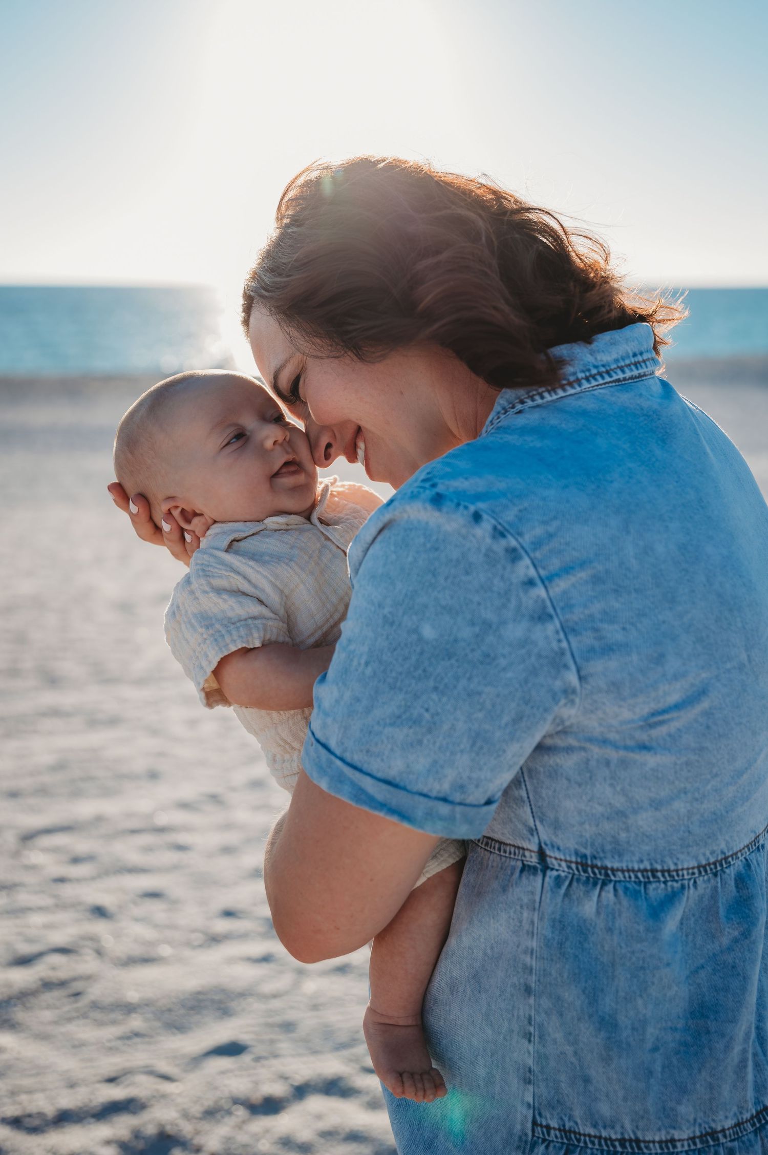 A parent in denim embraces a baby tenderly on a sunny 30A beach.
