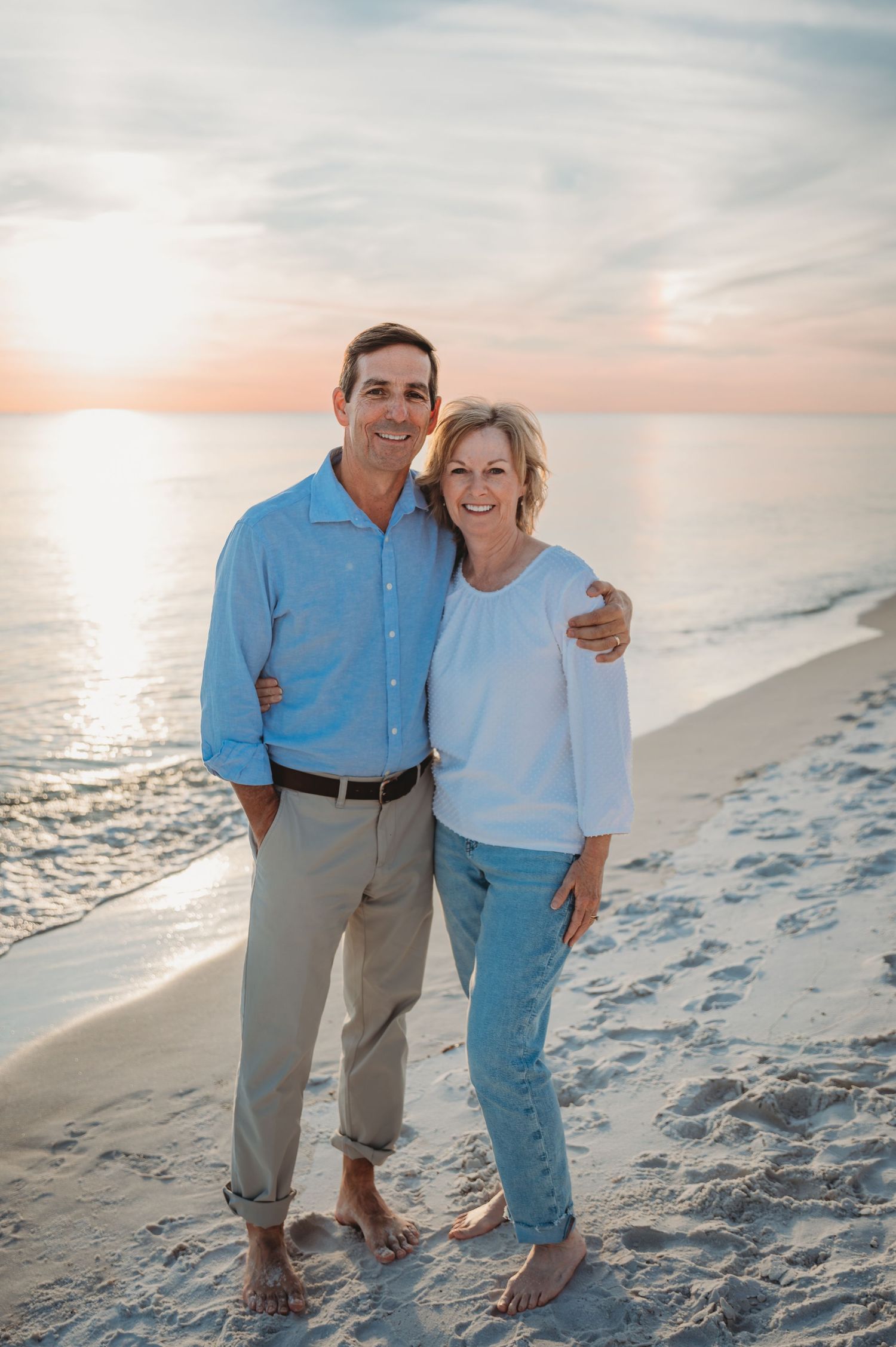 Two people in casual blue and white outfits walk together on a sandy beach at sunset with ocean waves in background in 30A.