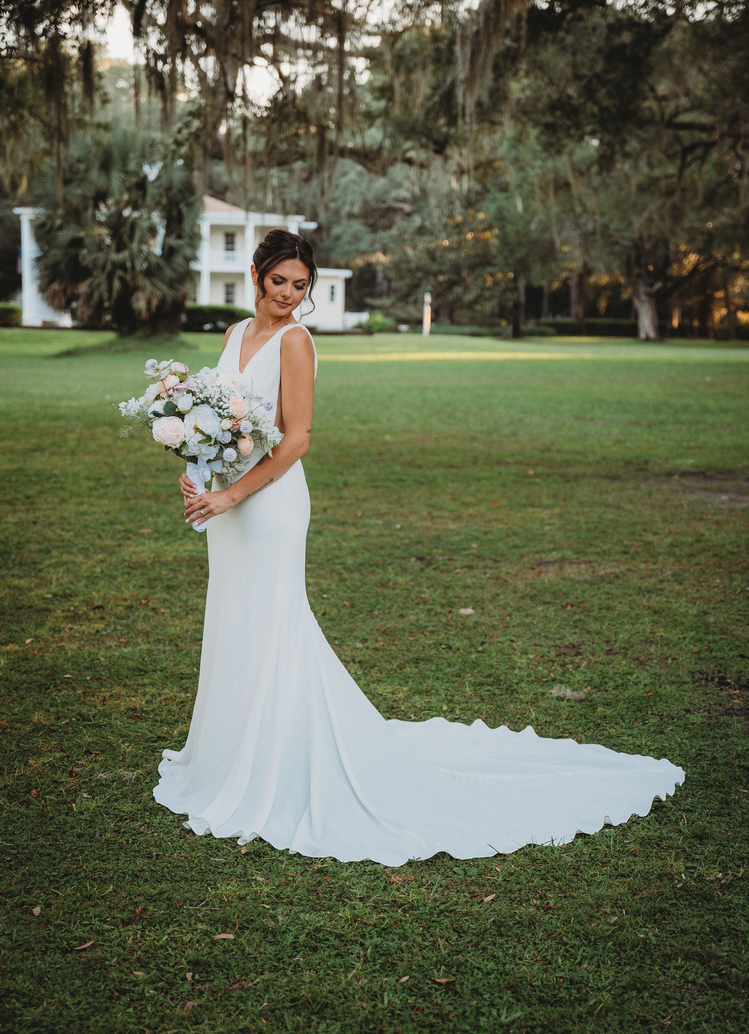 A stunning white wedding dress with a flowing train photographed on a lush green lawn during a Panama City Beach wedding.