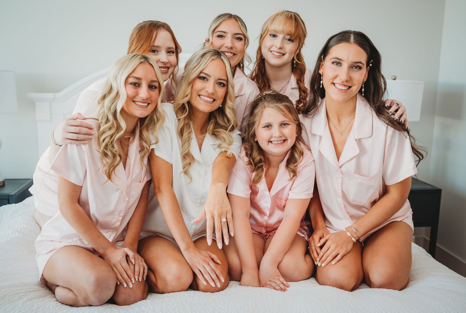 A group of bridesmaids in pink and white robes pose together on a bed during a 30A wedding.