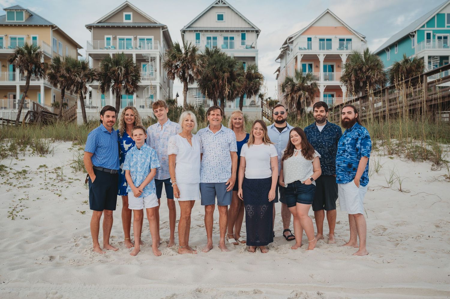 A group stands together on a beach with colorful coastal beach houses and palm trees in the background at dusk in Panama City Beach.