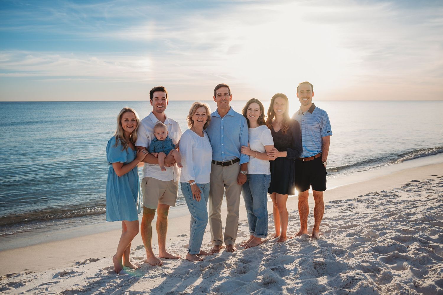 A group of people standing together on a sunny 30A beach at sunset with the ocean and blue sky in the background.