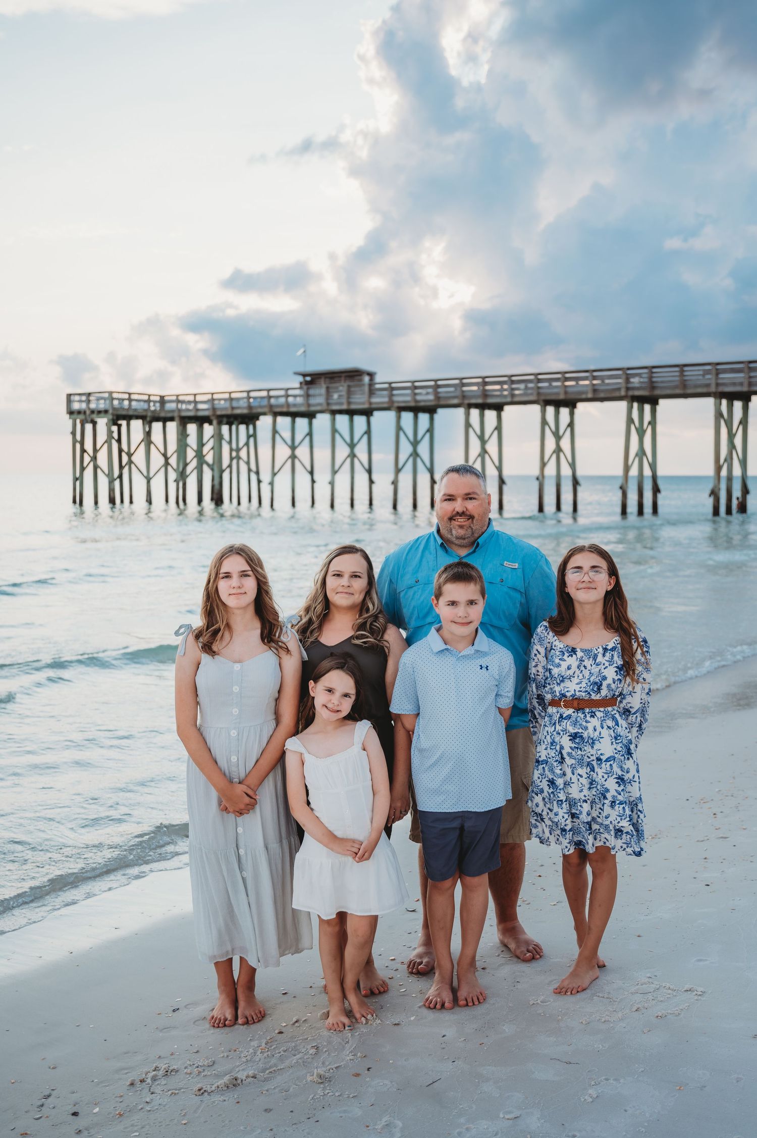 A family group poses together on the beach at sunset with a wooden pier in the background in Panama City Beach.