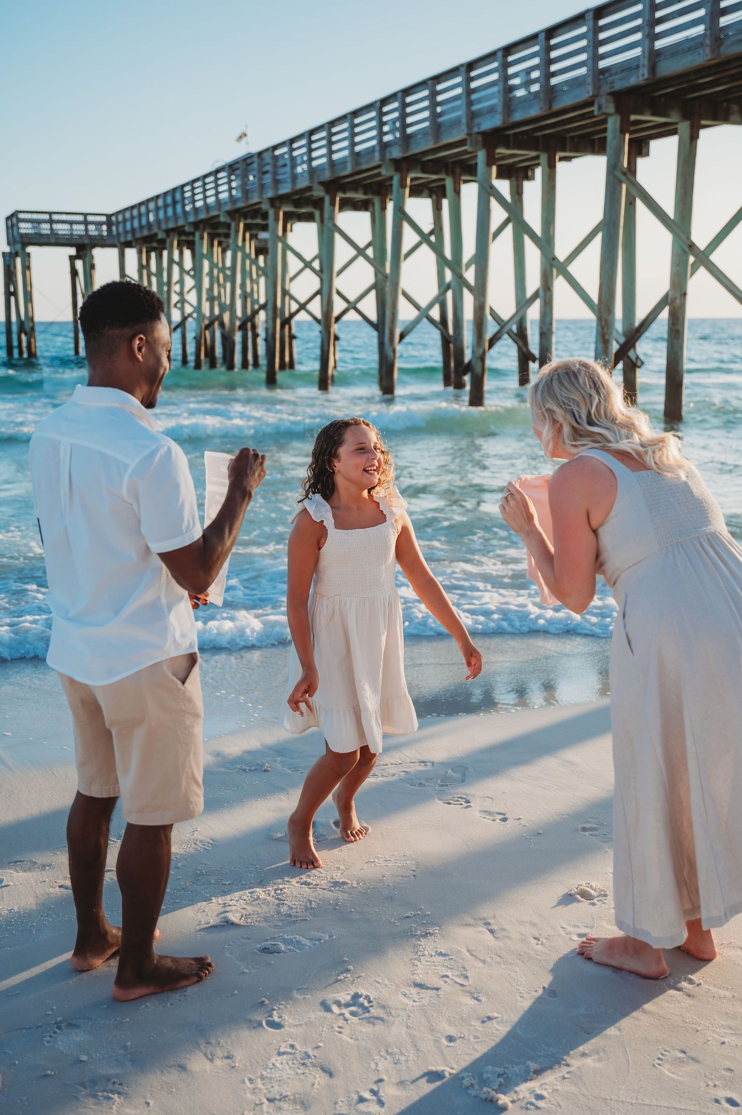 People in white attire having a fun, candid moment by an oceanfront pier on a sandy beach in Panama City Beach.