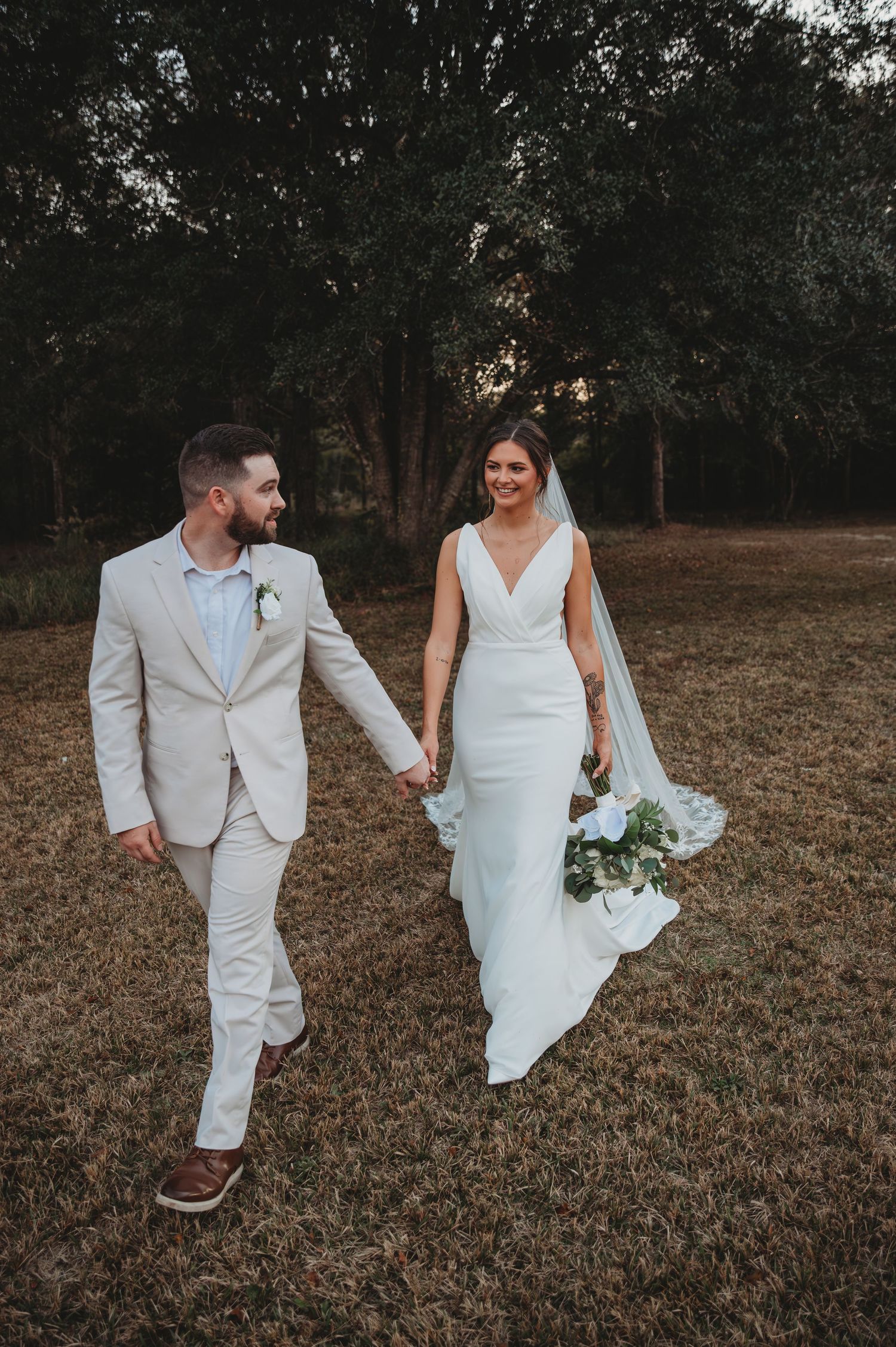 A couple in wedding attire walks together through a rustic outdoor field during golden hour during a Panama City Beach wedding.