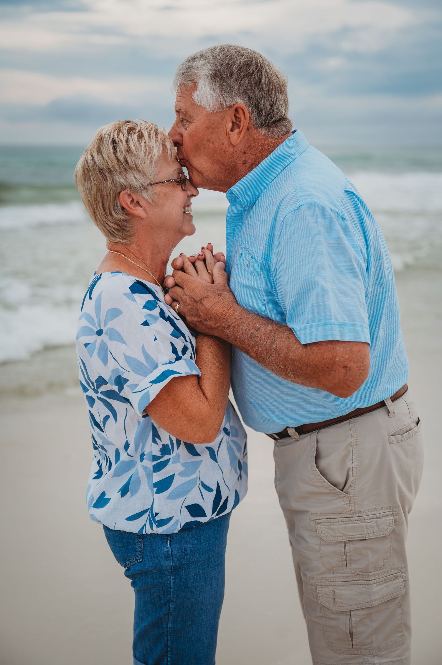 Elderly couple embraces lovingly on a cloudy beach with waves in the background in Panama City Beach.