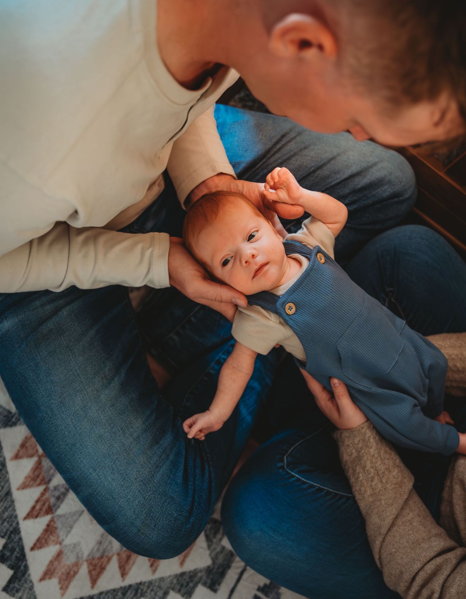 A baby wearing a blue onesie lies on a patterned rug while being held by someone in denim during a newborn session in Panama City.