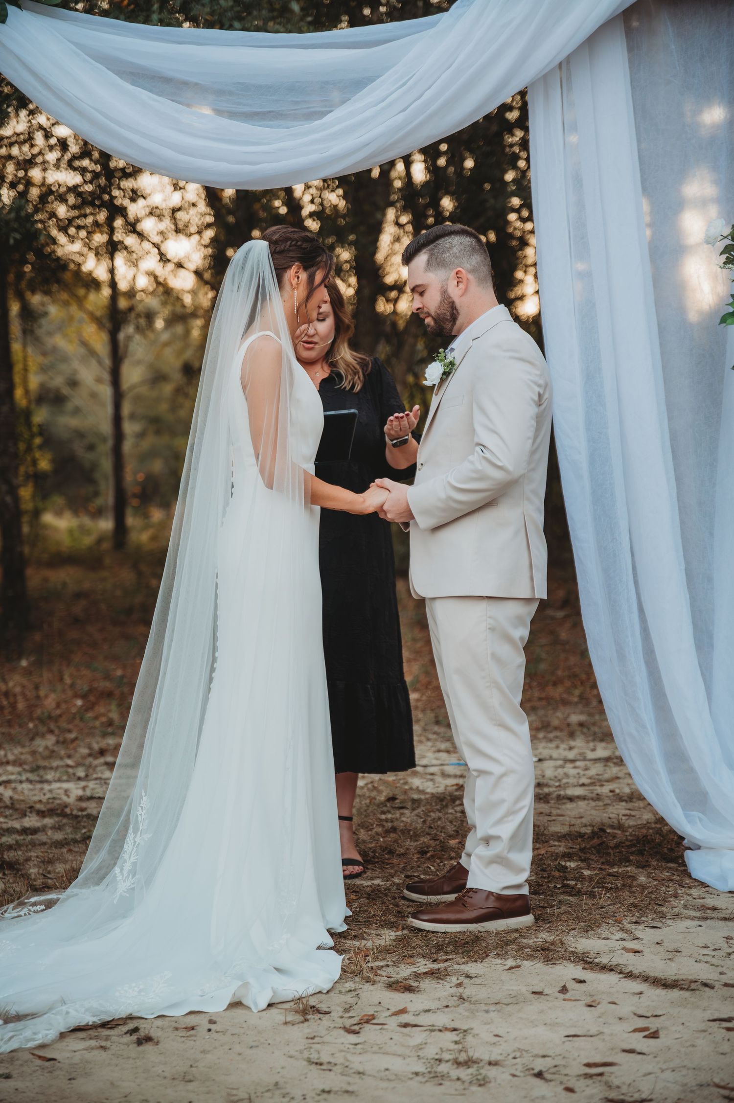 A wedding ceremony takes place under flowing white fabric drapes in Panama City Beach at sunset.