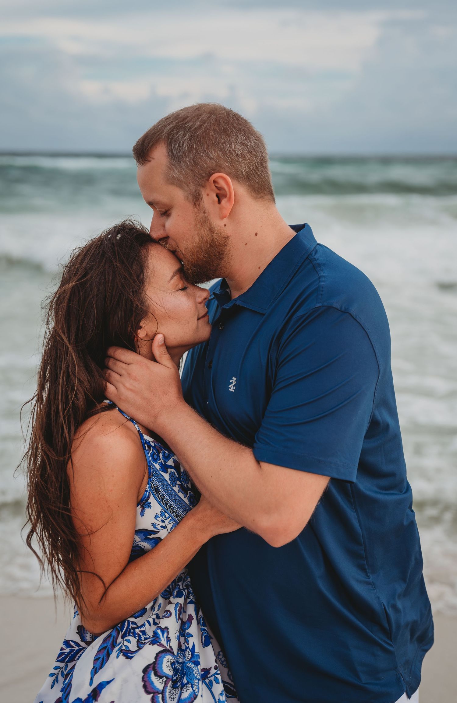 A couple shares romantic kisses on a beach with crashing waves in the background in Panama City Beach.