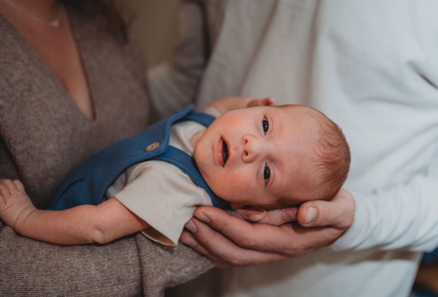 Baby in white onesie lying on soft bedding while being gently touched by adult hands during a newborn session in Panama City.