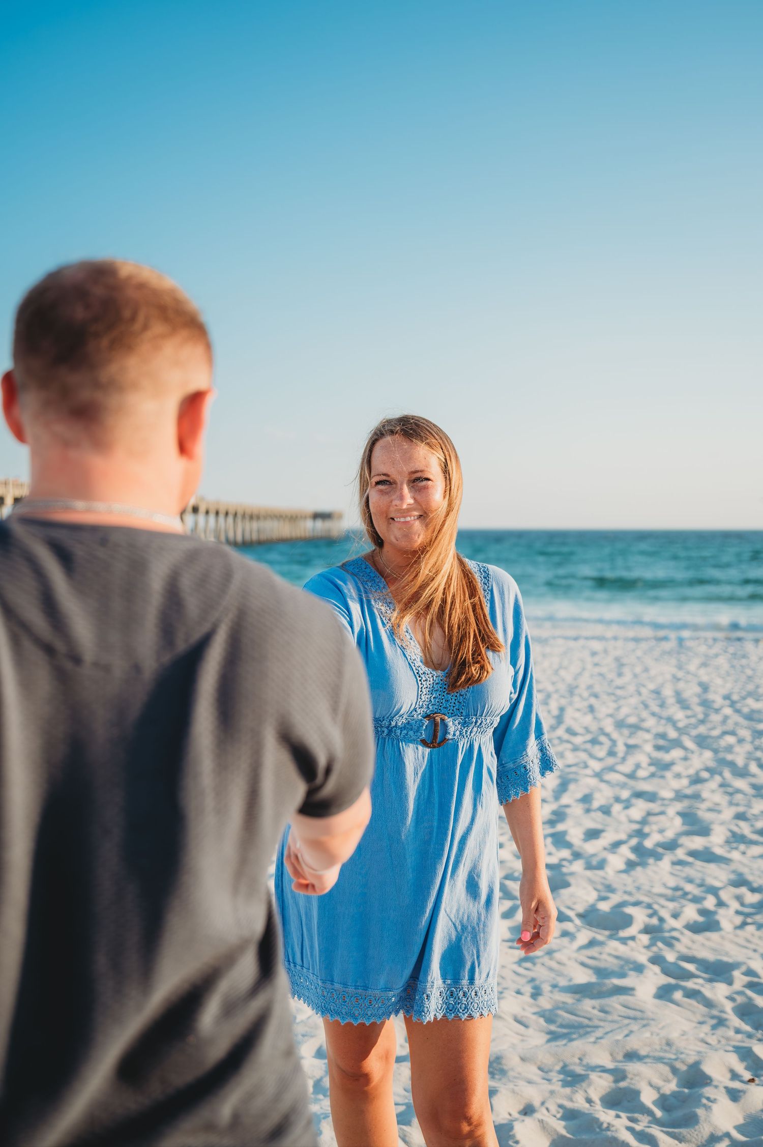Happy couple walking hand in hand on a pristine white sandy beach with blue ocean waves in the background in Panama City Beach.