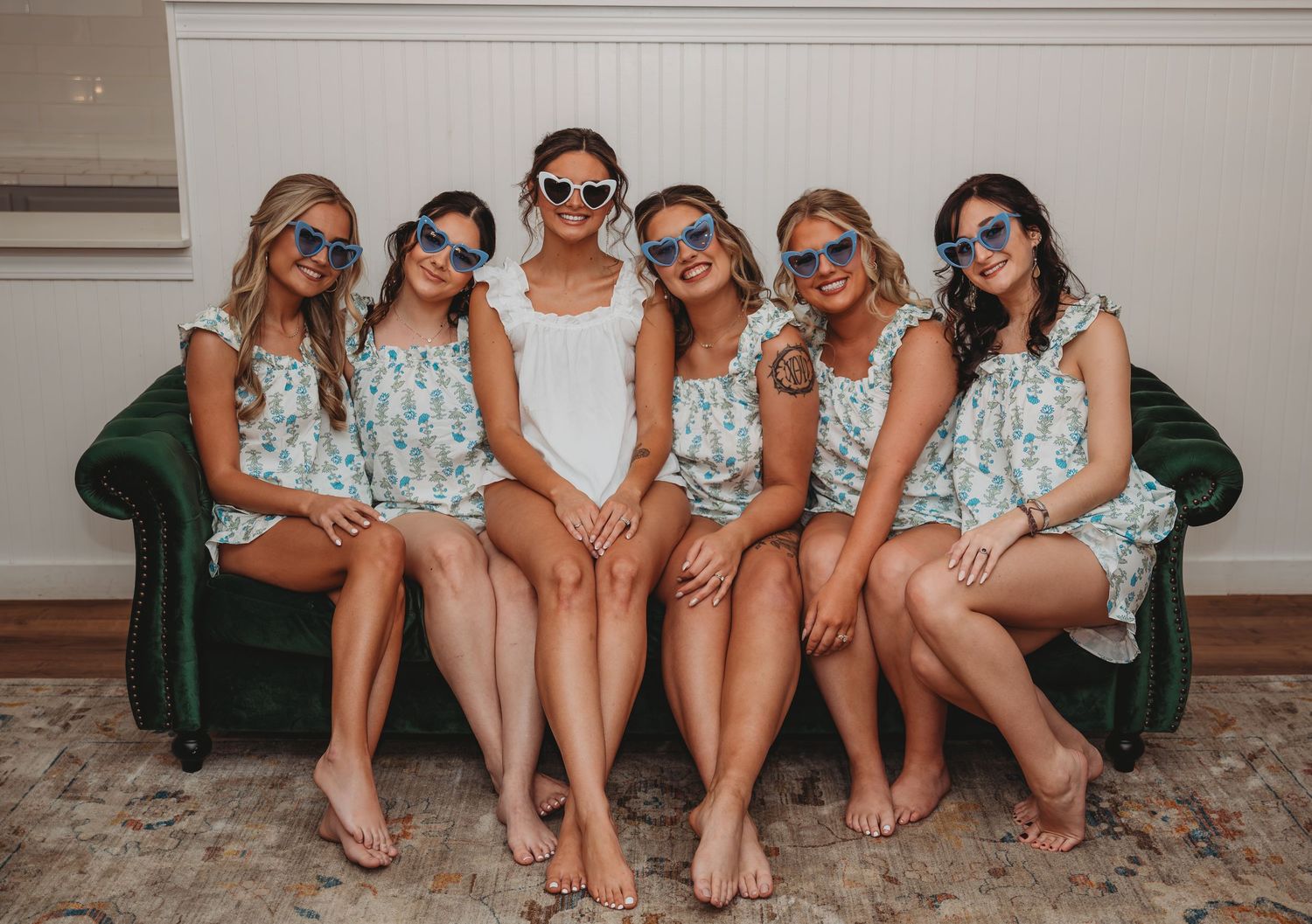 Bridesmaids wearing matching floral dresses and sunglasses sit together during a Panama City Beach wedding.