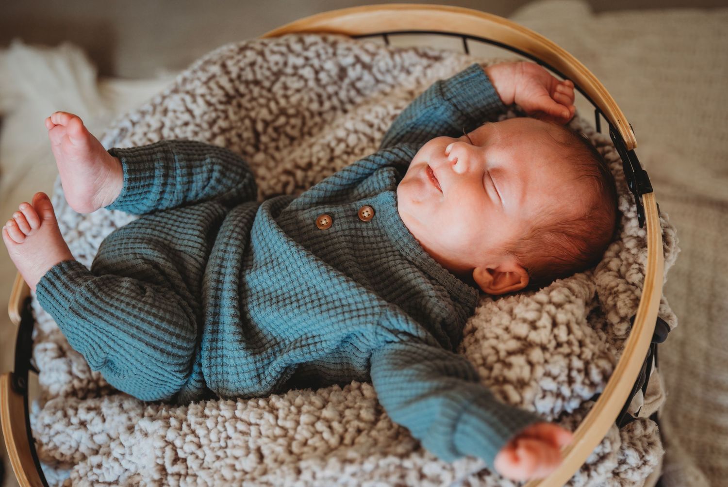 A newborn baby wearing blue sleepwear rests peacefully in a cozy woven basket with textured blanket during a newborn session in Panama City.