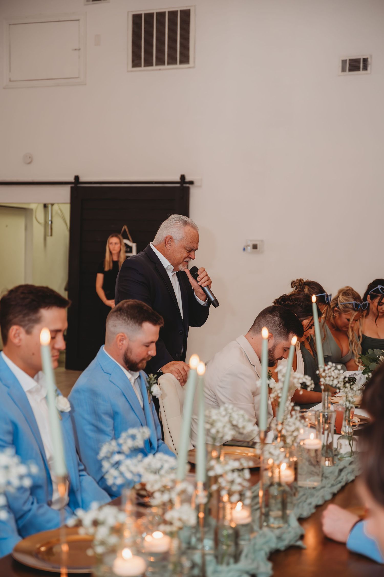 Groomsmen seated at a long candlelit dinner table wearing light blue jackets during a Panama City Beach wedding.