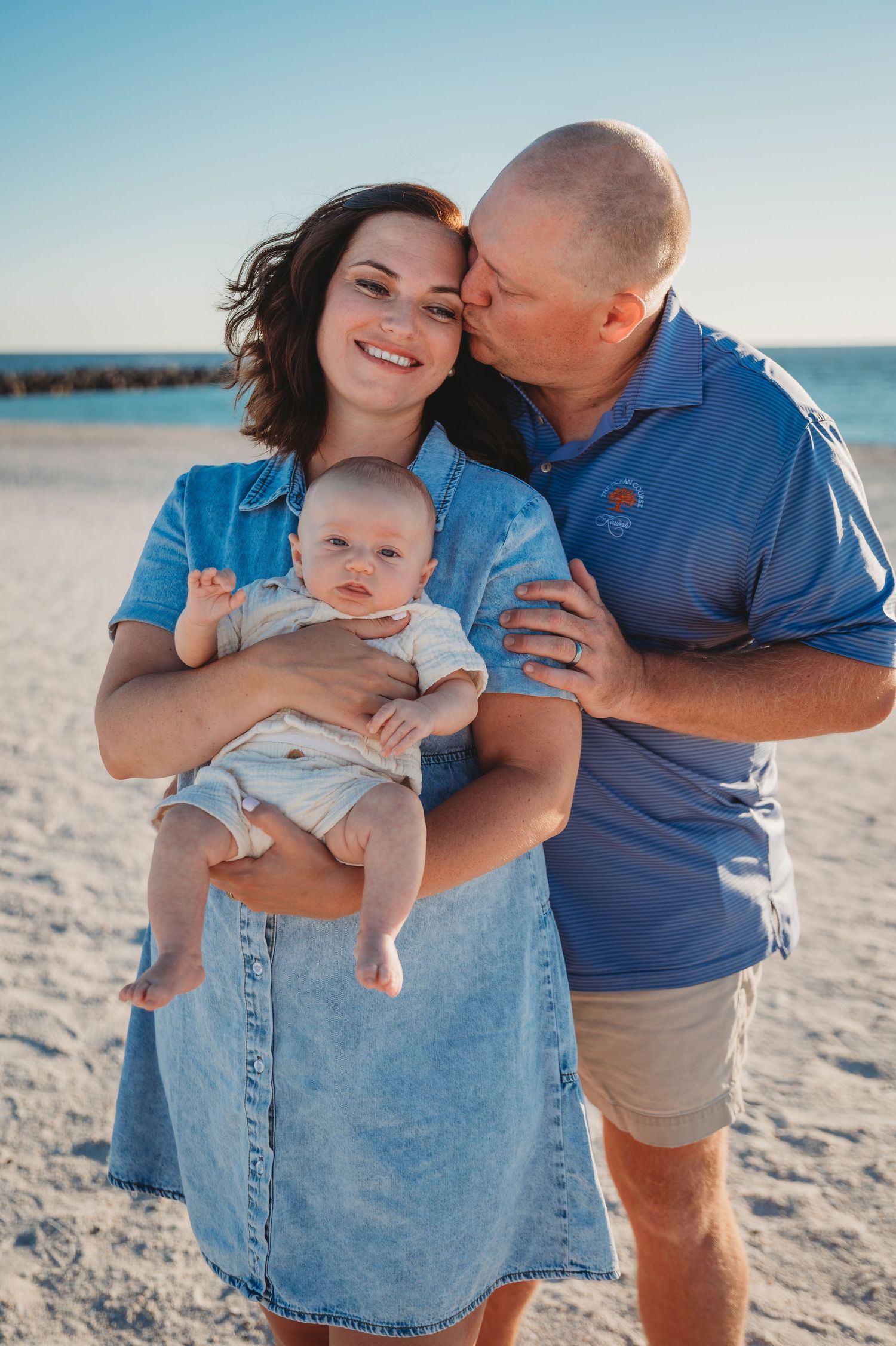 A family shares tender moments together on a sunny St. Andrew's beach, wearing coordinating blue outfits.