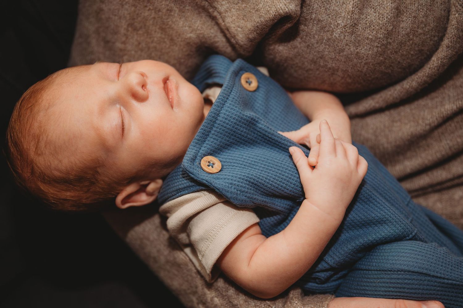 Baby sleeping peacefully in blue onesie on gray textured blanket with stuffed animal nearby during a newborn session in Panama City.