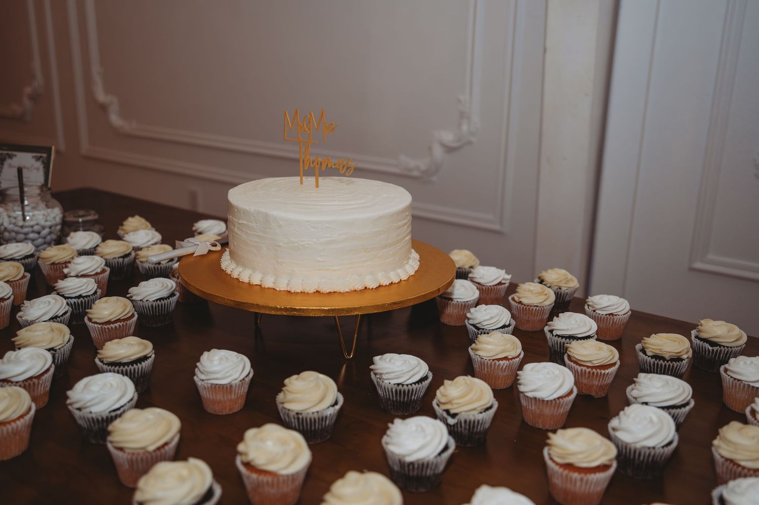 White wedding cake displayed with matching cupcakes arranged on a wooden table at a reception during a Panama City Beach wedding.