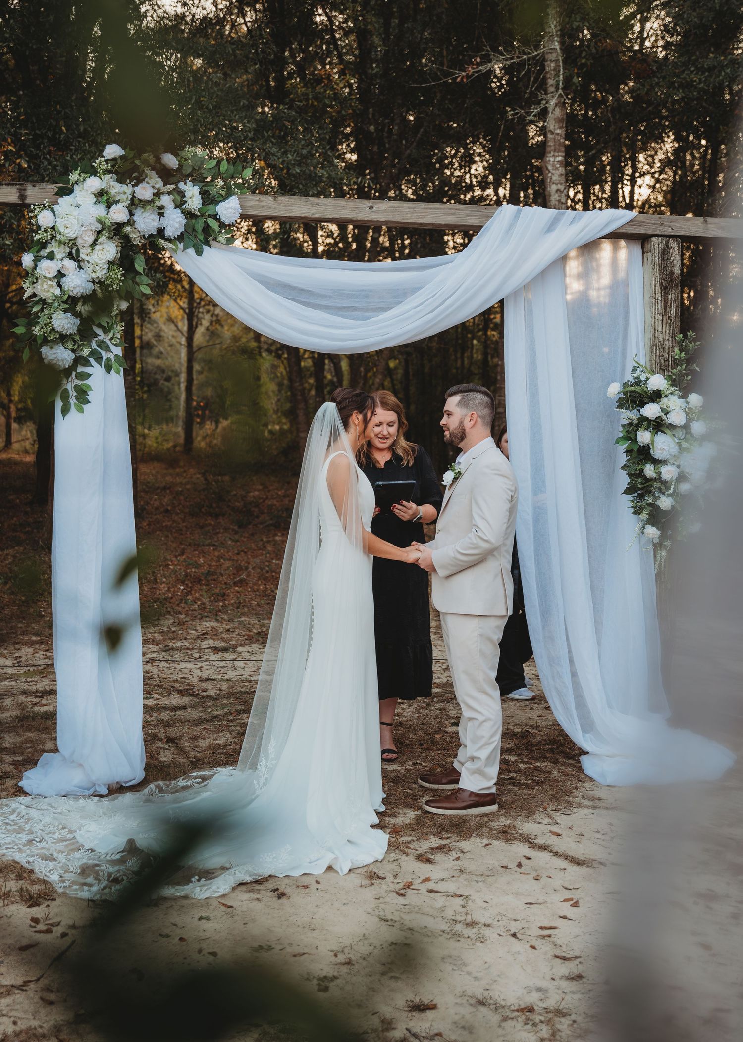 A romantic outdoor wedding ceremony under white flowing drapery and natural greenery at sunset in Panama City Beach.