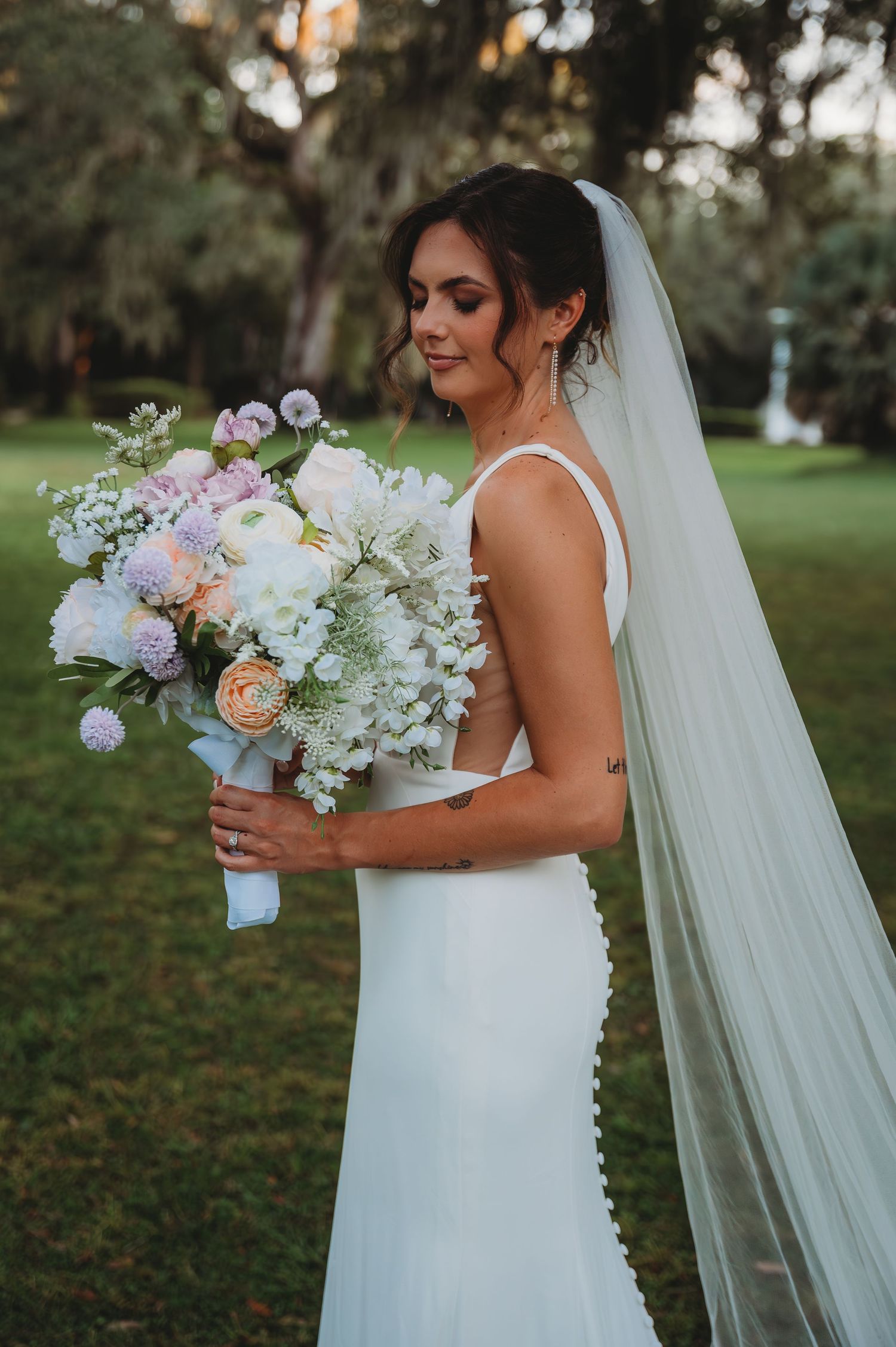 Bride in a white wedding dress holds a beautiful bouquet of white and peach flowers with a flowing veil during a Panama City Beach wedding.