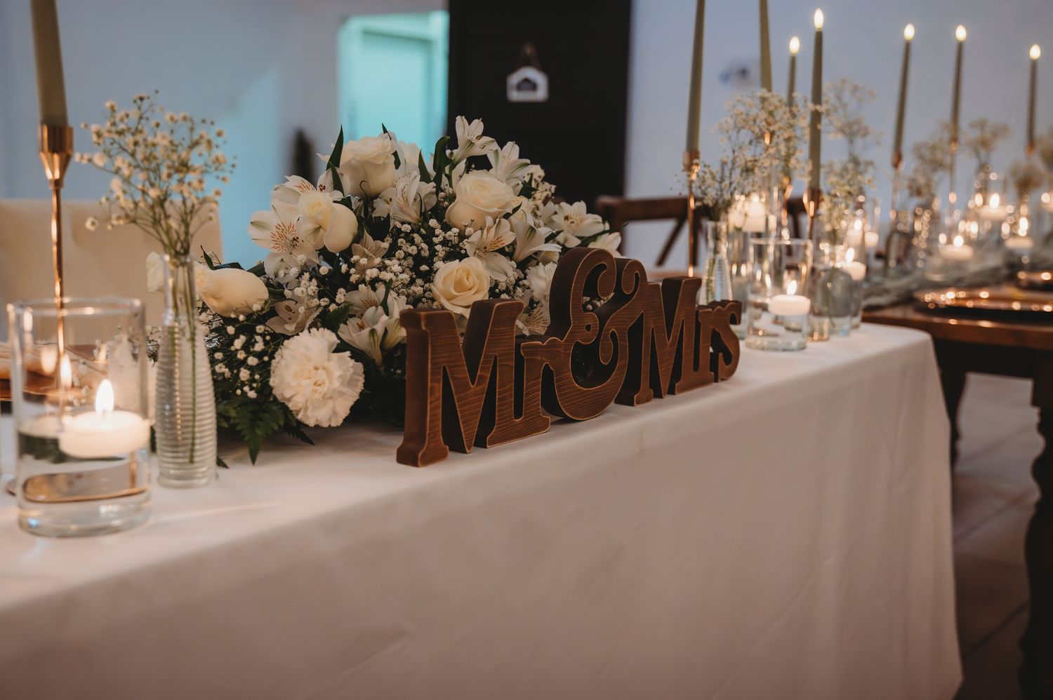 Wedding reception table setup with white floral centerpieces, candles and Mr & Mrs sign in gold lettering during a Panama City Beach.