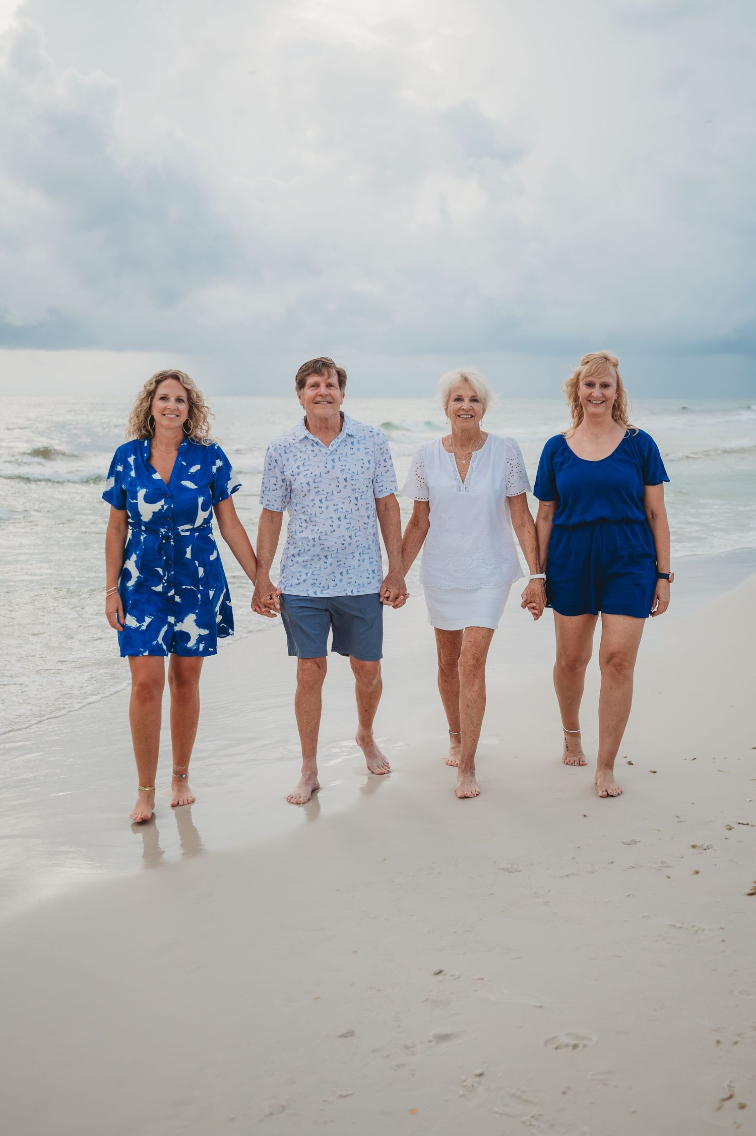 Four people walking together and holding hands on a sandy beach with cloudy sky and ocean in the background in Panama City Beach.