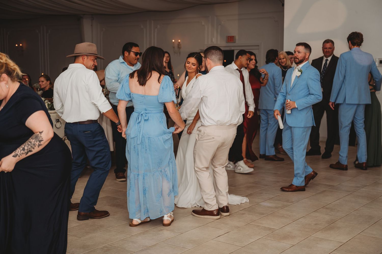 Wedding guests in light blue and white attire dance together on a reception dance floor during a Panama City Beach wedding.