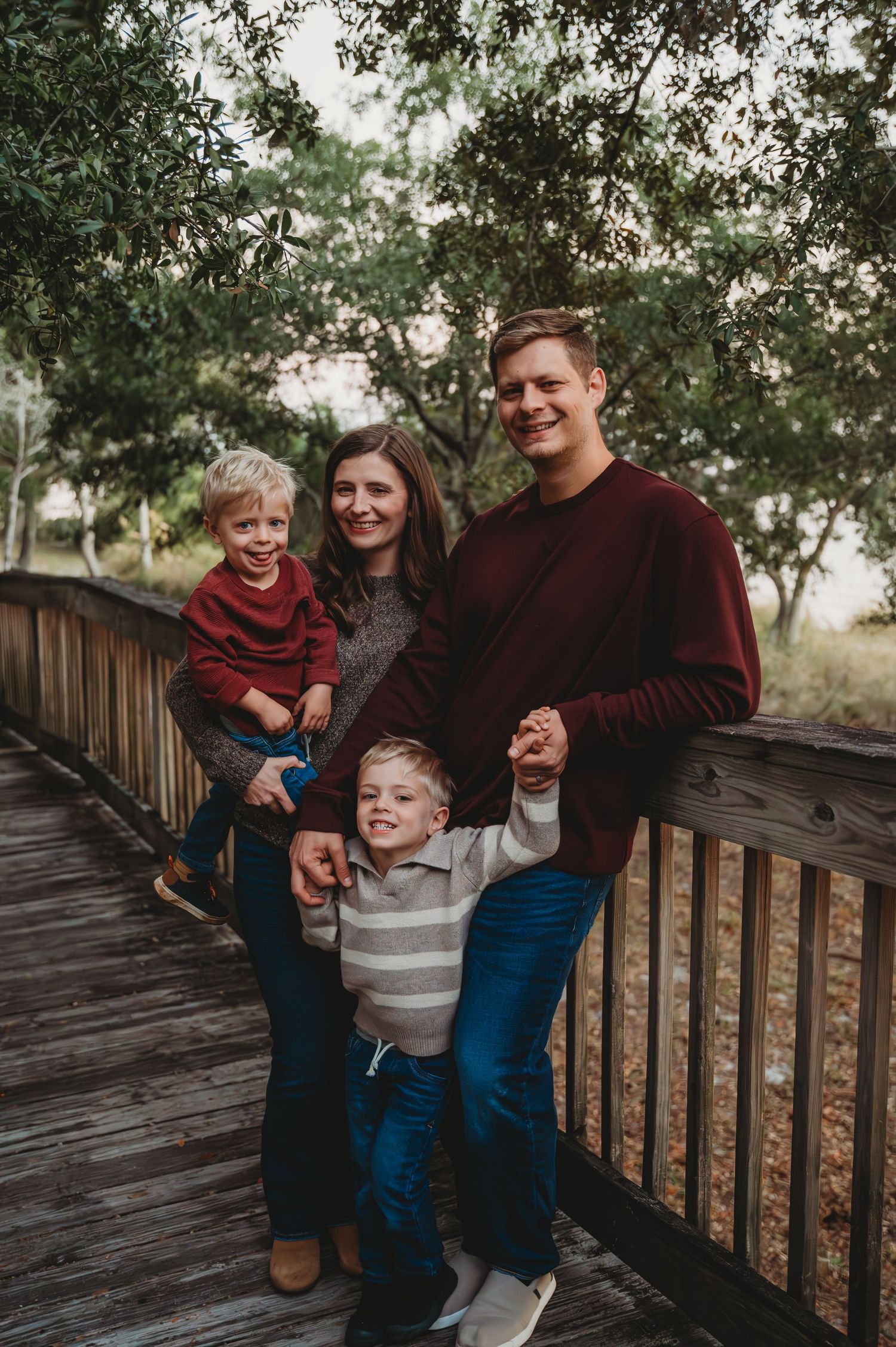 A family in burgundy and neutral tones shares candid moments together on a wooden deck surrounded by trees in Panama City.