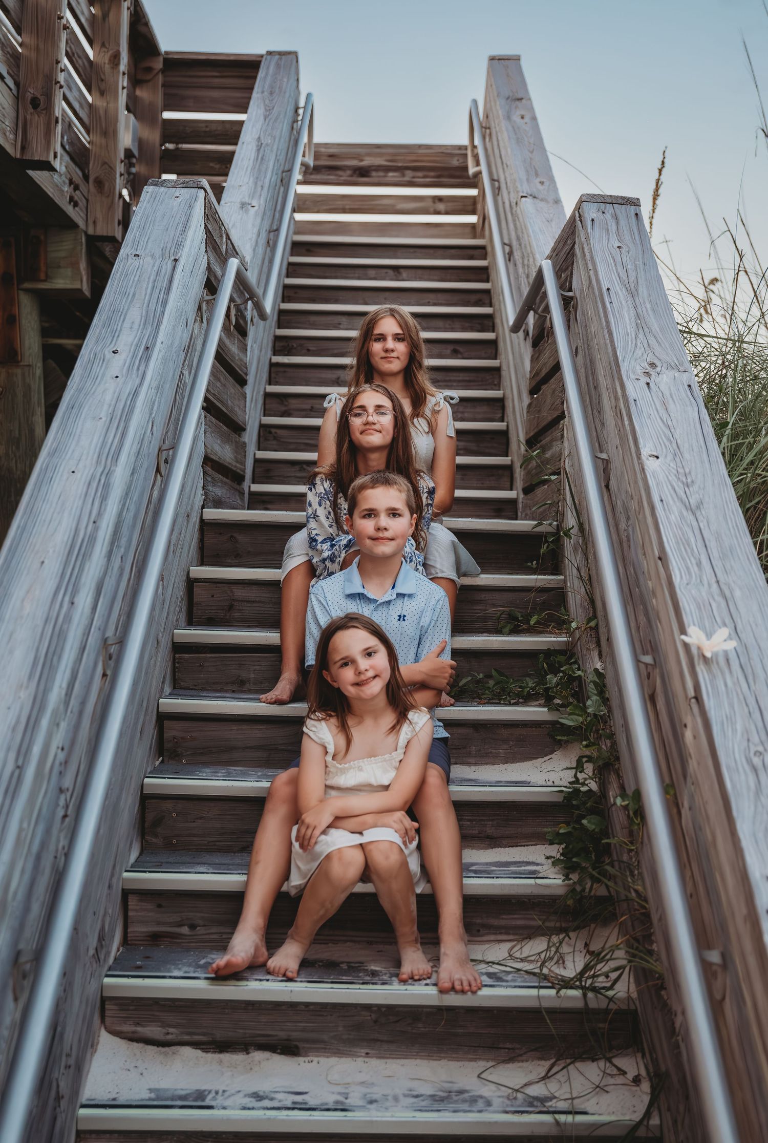 Four siblings sitting on a rustic wooden outdoor staircase during golden hour in Panama City Beach.