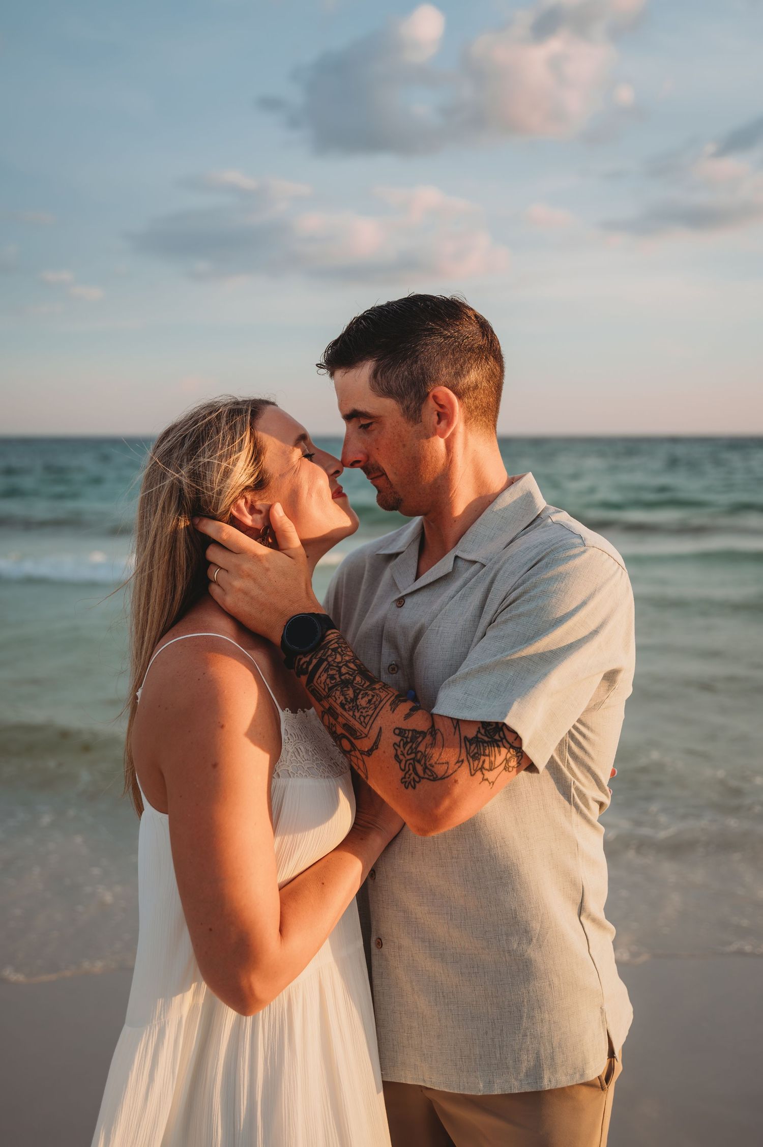 A romantic couple shares an intimate moment at sunset on a beach with ocean waves and cloudy sky in the background in Panama City Beach.
